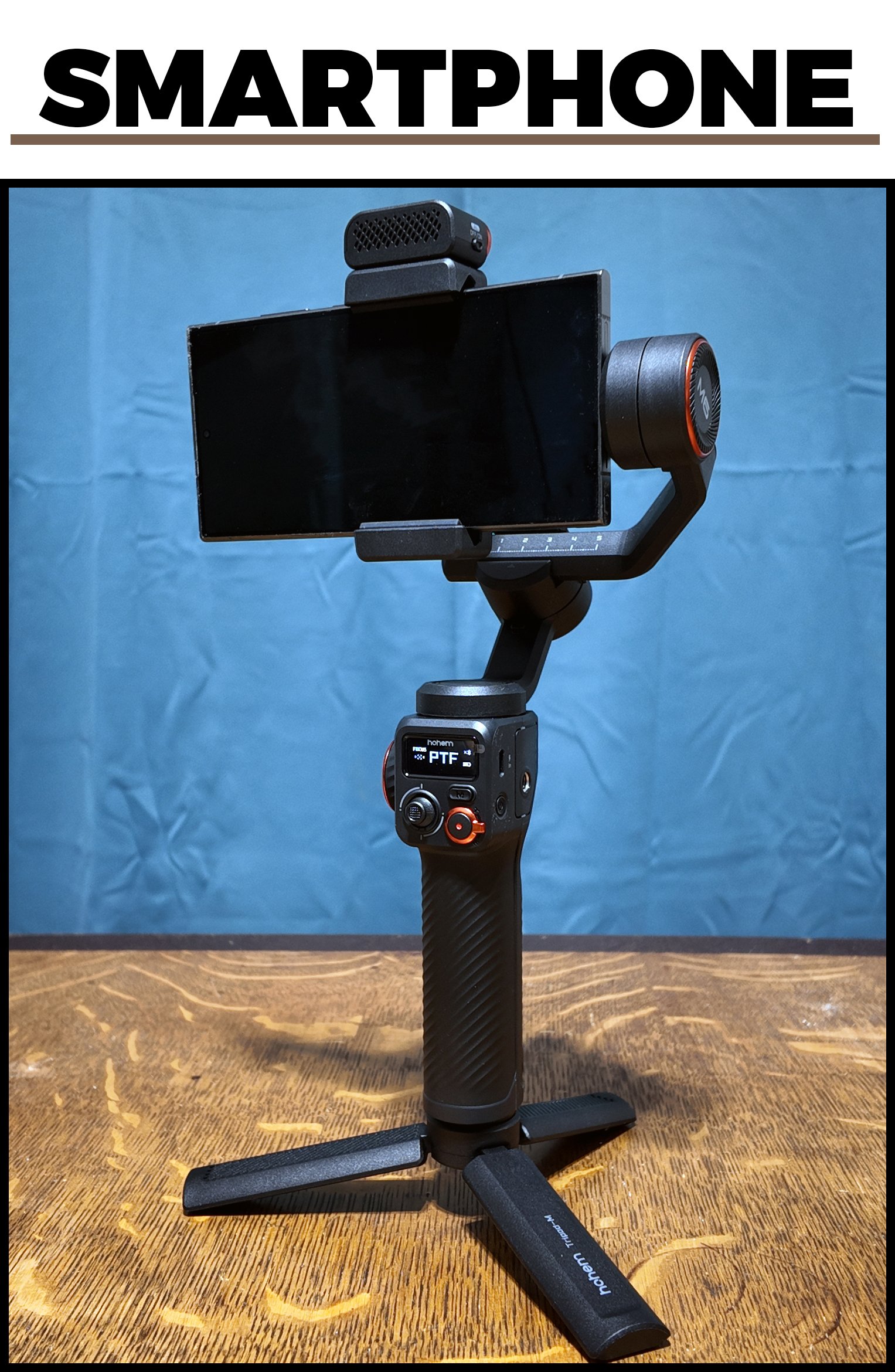 A handheld gimbal stabilizer with a mounted smartphone, displayed on a wooden surface against a blue backdrop.