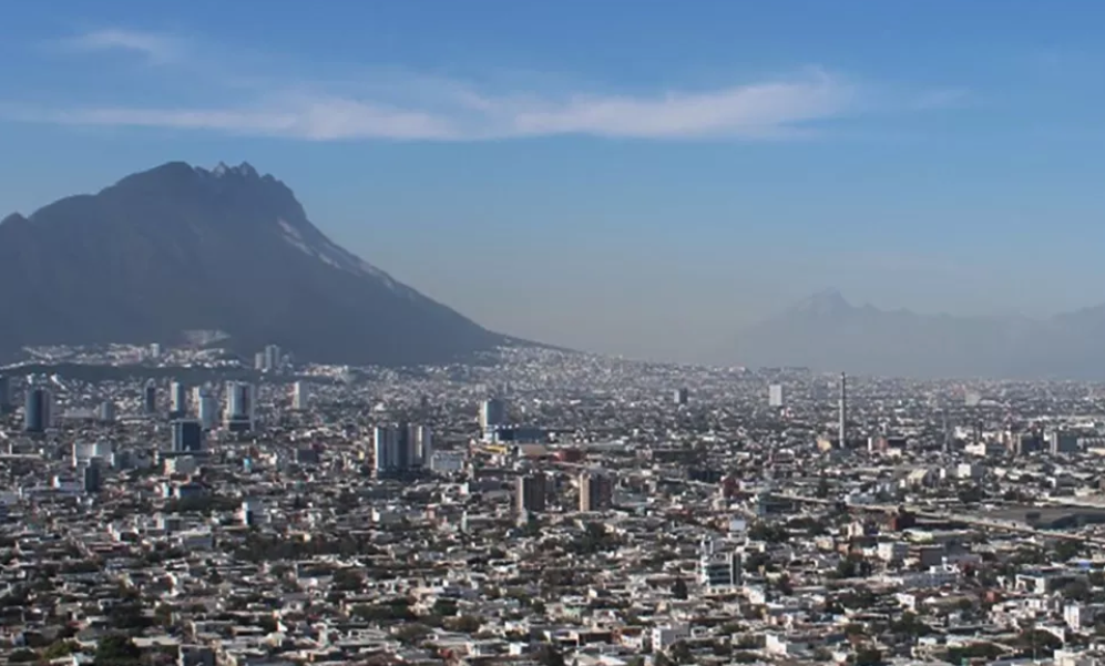 Wide cityscape with densely packed buildings and high-rises, with a large volcanic mountain in the background under a blue sky.