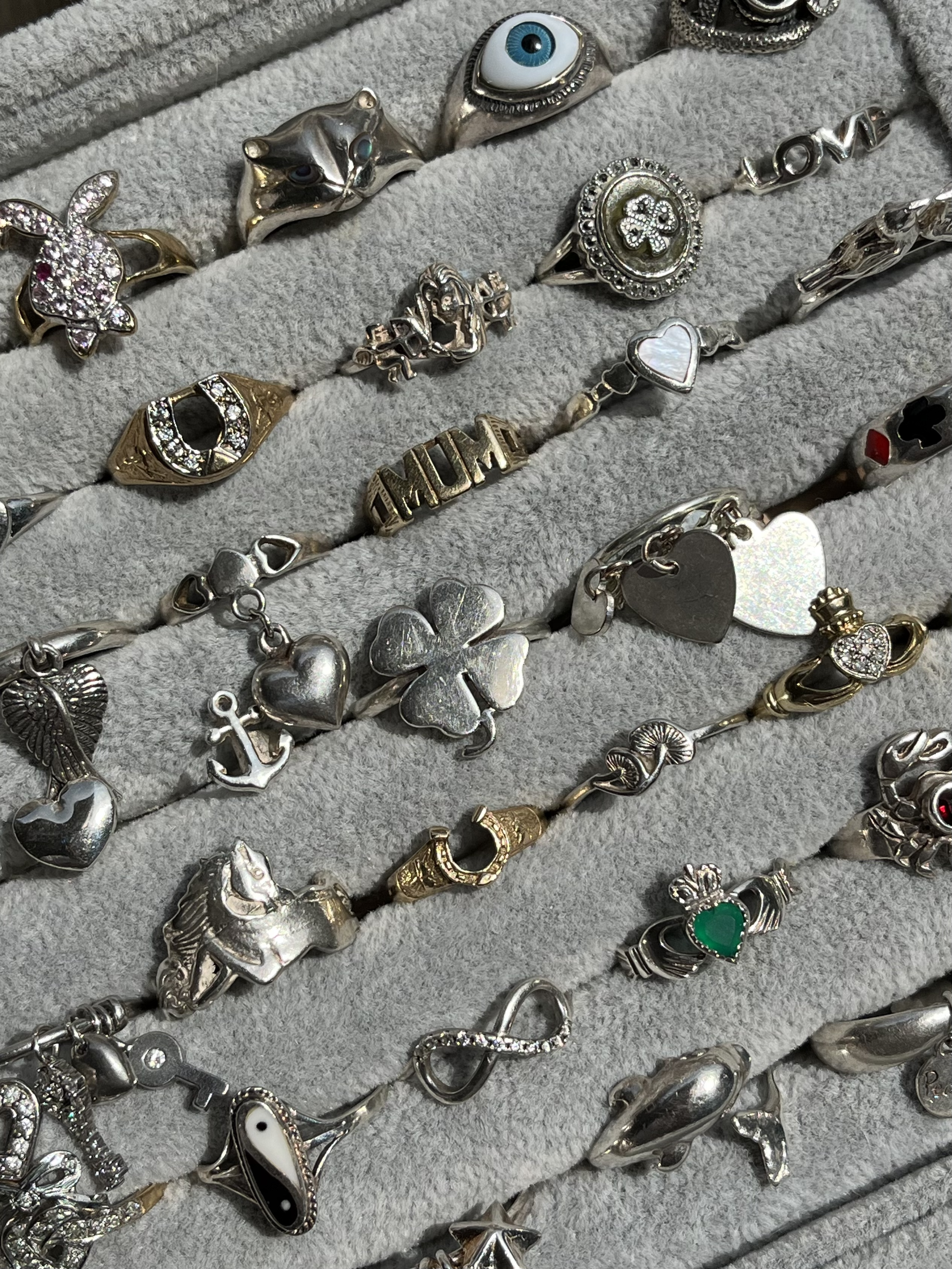 Close-up tray of vintage silver charms and rings, featuring heart, clover, anchor, and sentimental designs from Sorrell Jewels.