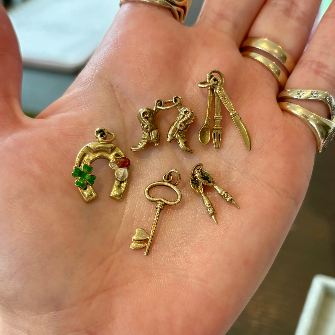 A hand holding a selection of small vintage gold charms, including lucky motifs and novelty designs, sourced