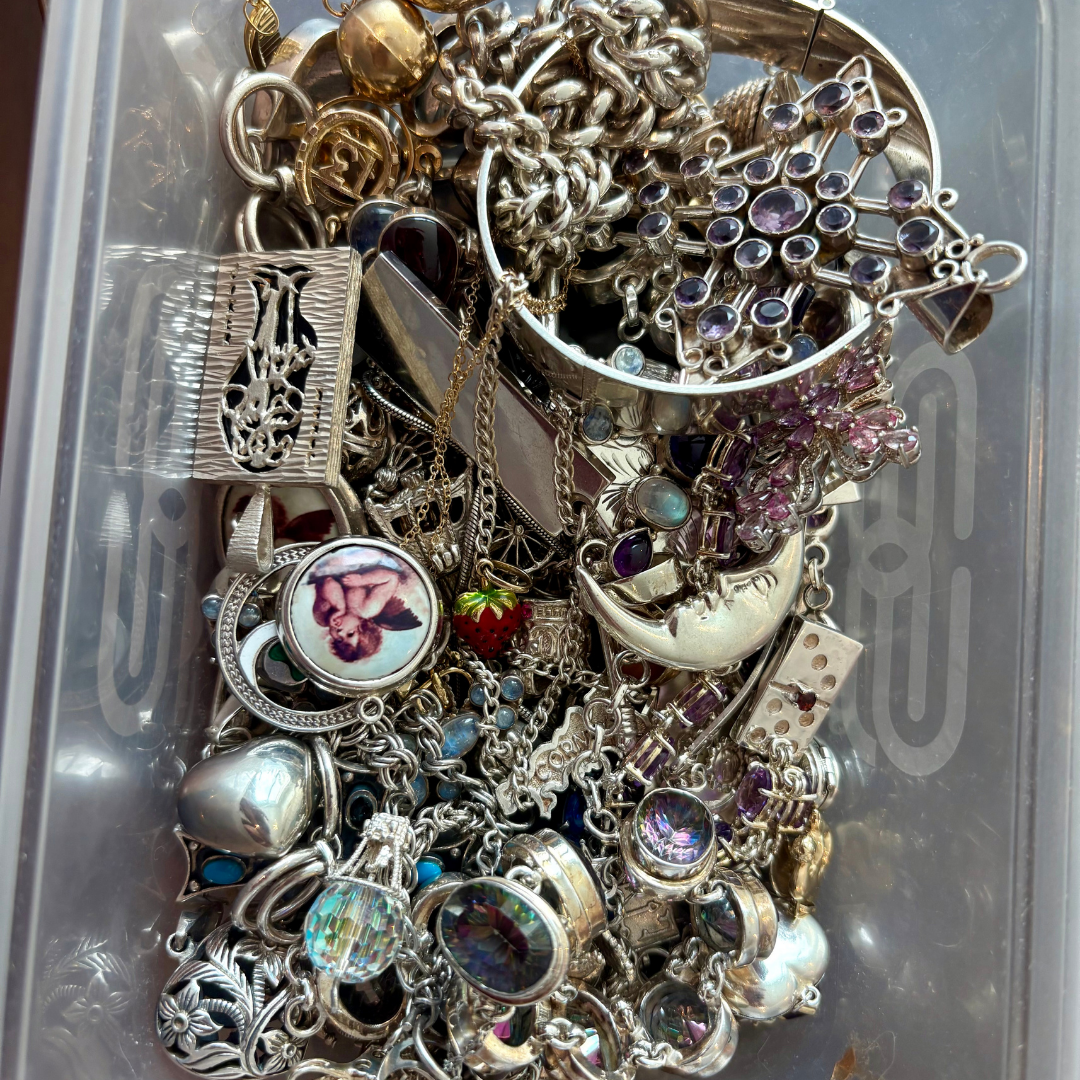 A plastic container filled with assorted vintage silver jewellery, chains and charms gathered together after a jewellery sourcing haul.