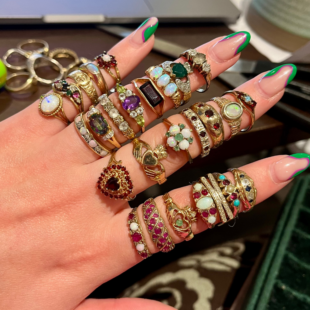 A hand stacked with vintage and antique gold rings set with opals and gemstones, showcasing a maximalist jewellery styling approach.