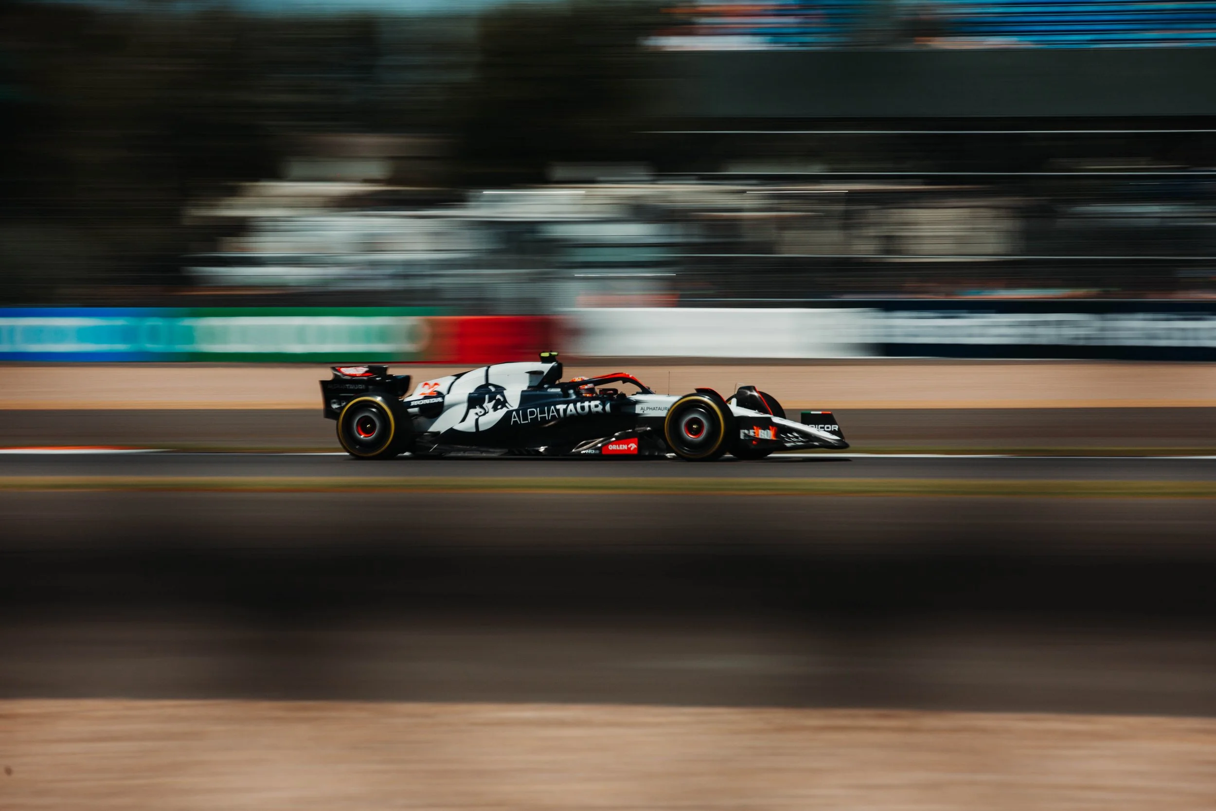 A black and white Formula race car driven by AlphaTauri speeding on a racetrack with motion blur background.