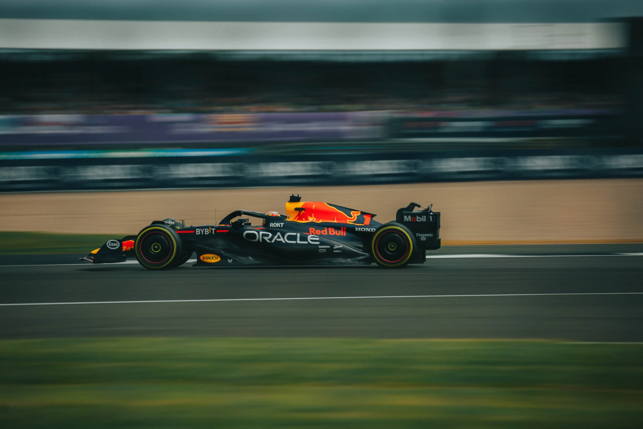A Red Bull Racing Formula 1 car speeding on a race track, with sponsors Oracle, Honda, and Red Bull visible, and a blurred background indicating high speed.