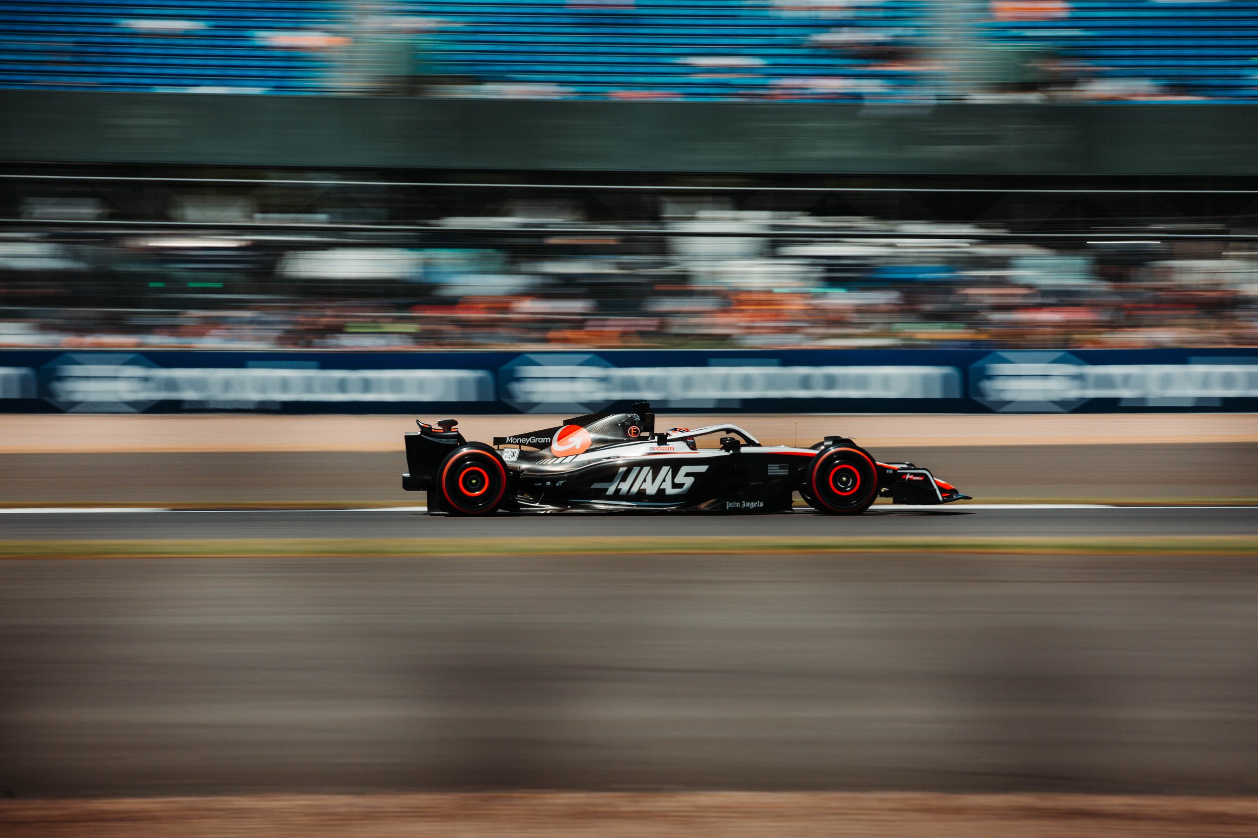 A black and white Formula 1 race car on the track during a race event, with a blurred background of spectators and facilities.