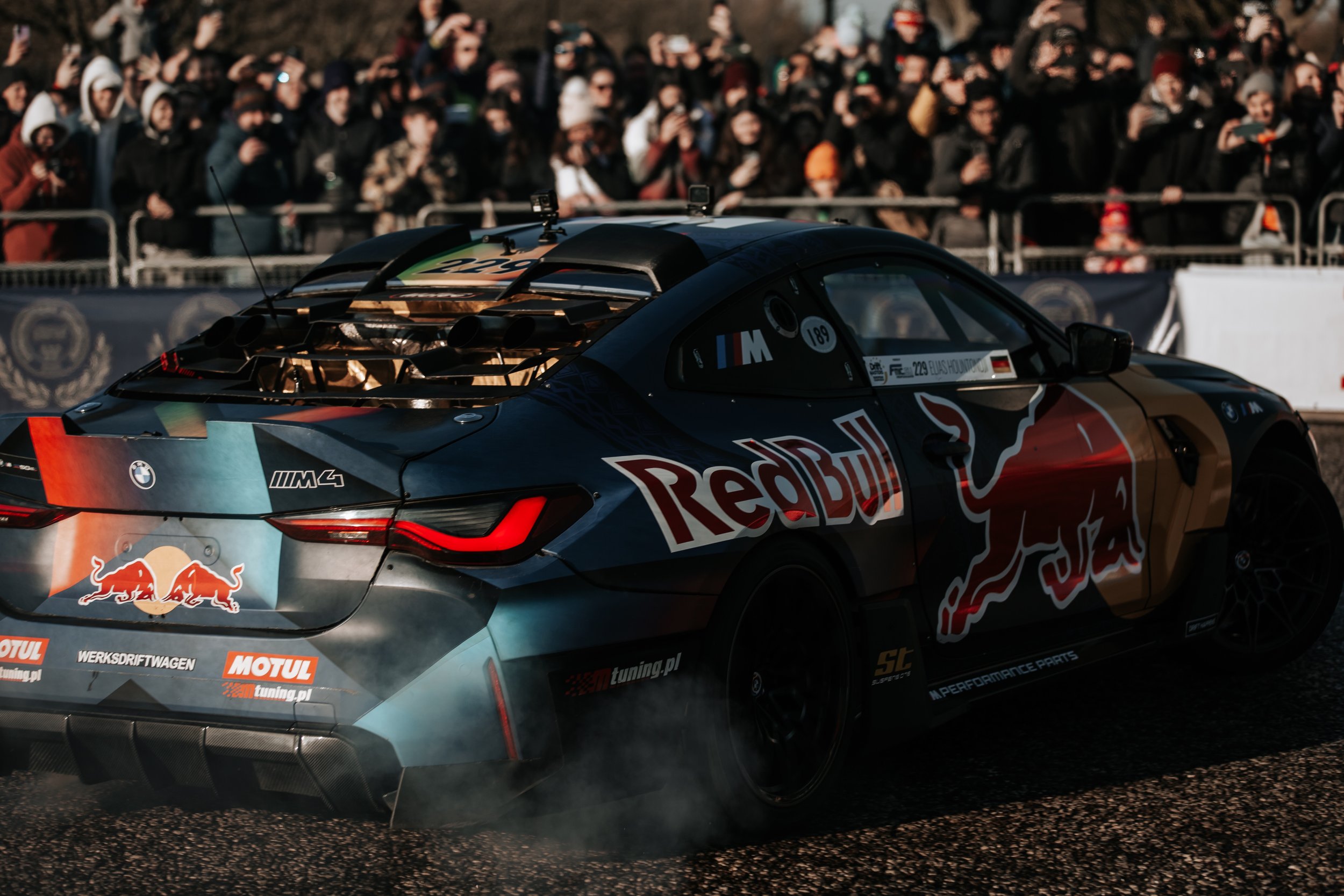 A racing car with Red Bull and BMW logos, on a racetrack with a crowd watching in the background.