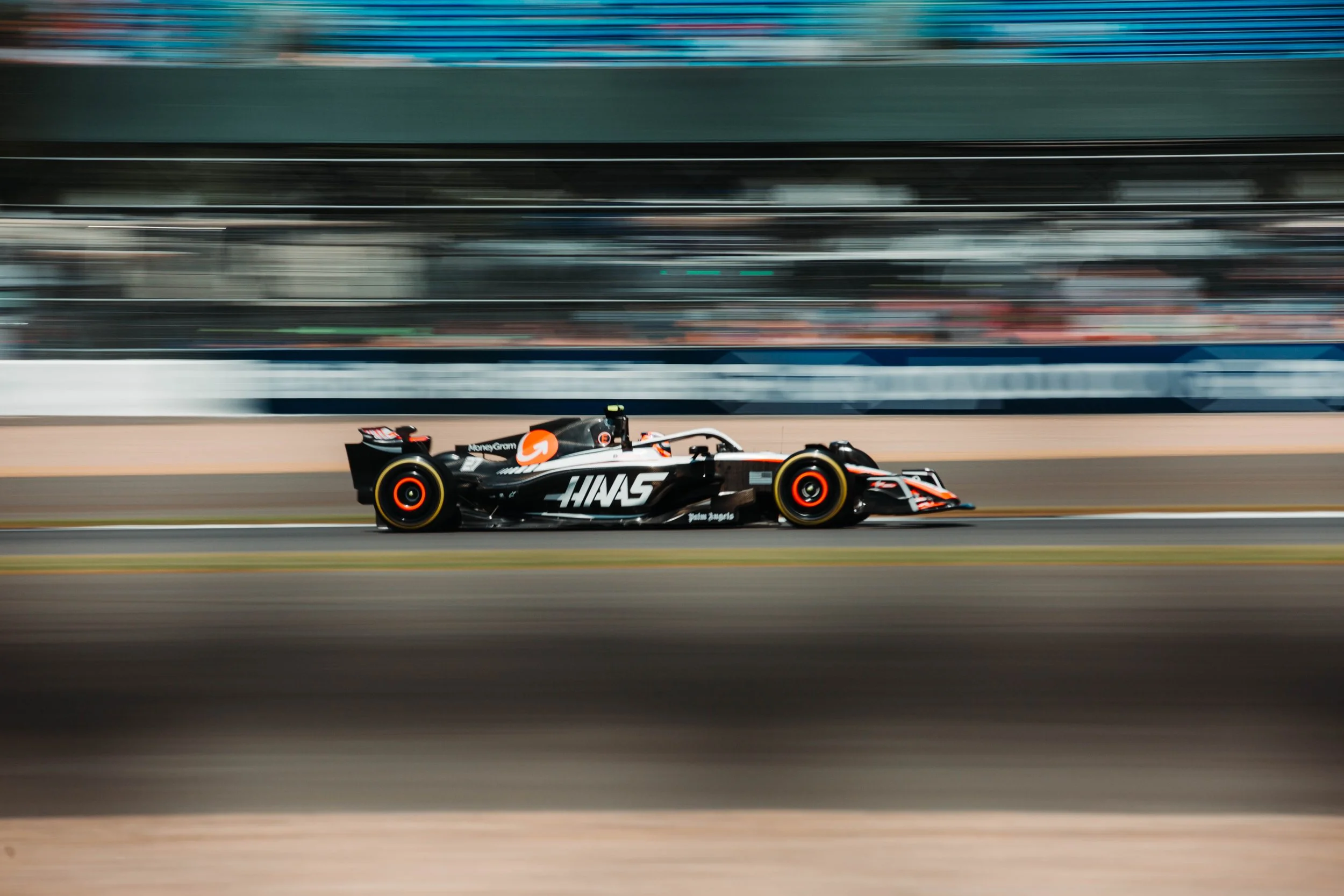 A black and white race car with Haas branding speeds on a racetrack, with blurred background indicating high speed.