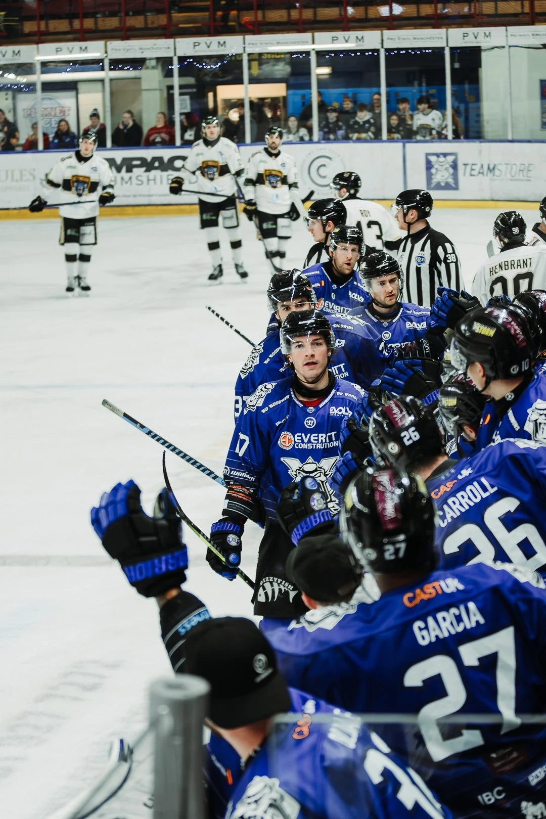 Ice hockey players shaking hands after a game on the ice rink, with spectators watching from behind the glass.