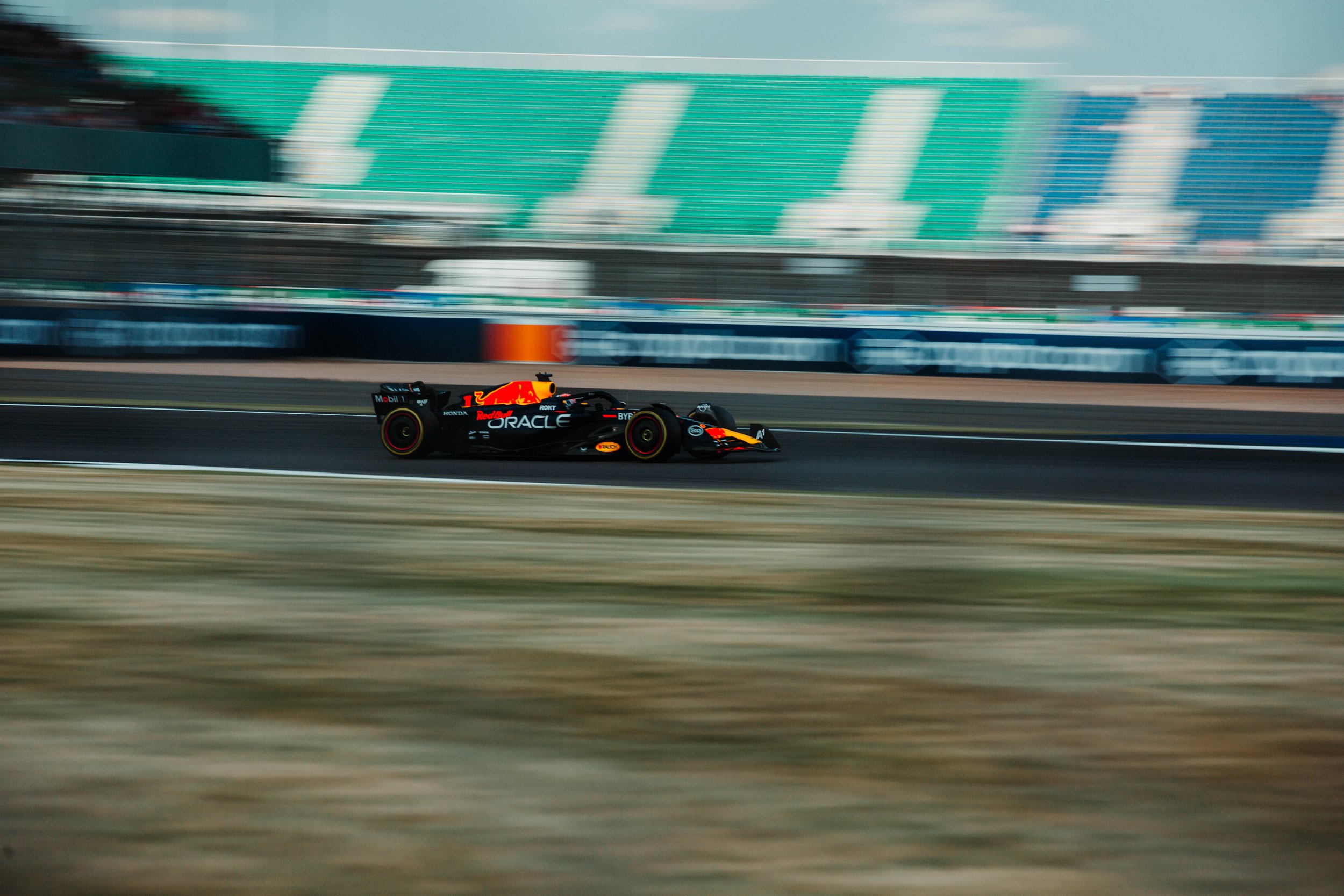 A race car moving at high speed on a race track with green grandstands in the background.