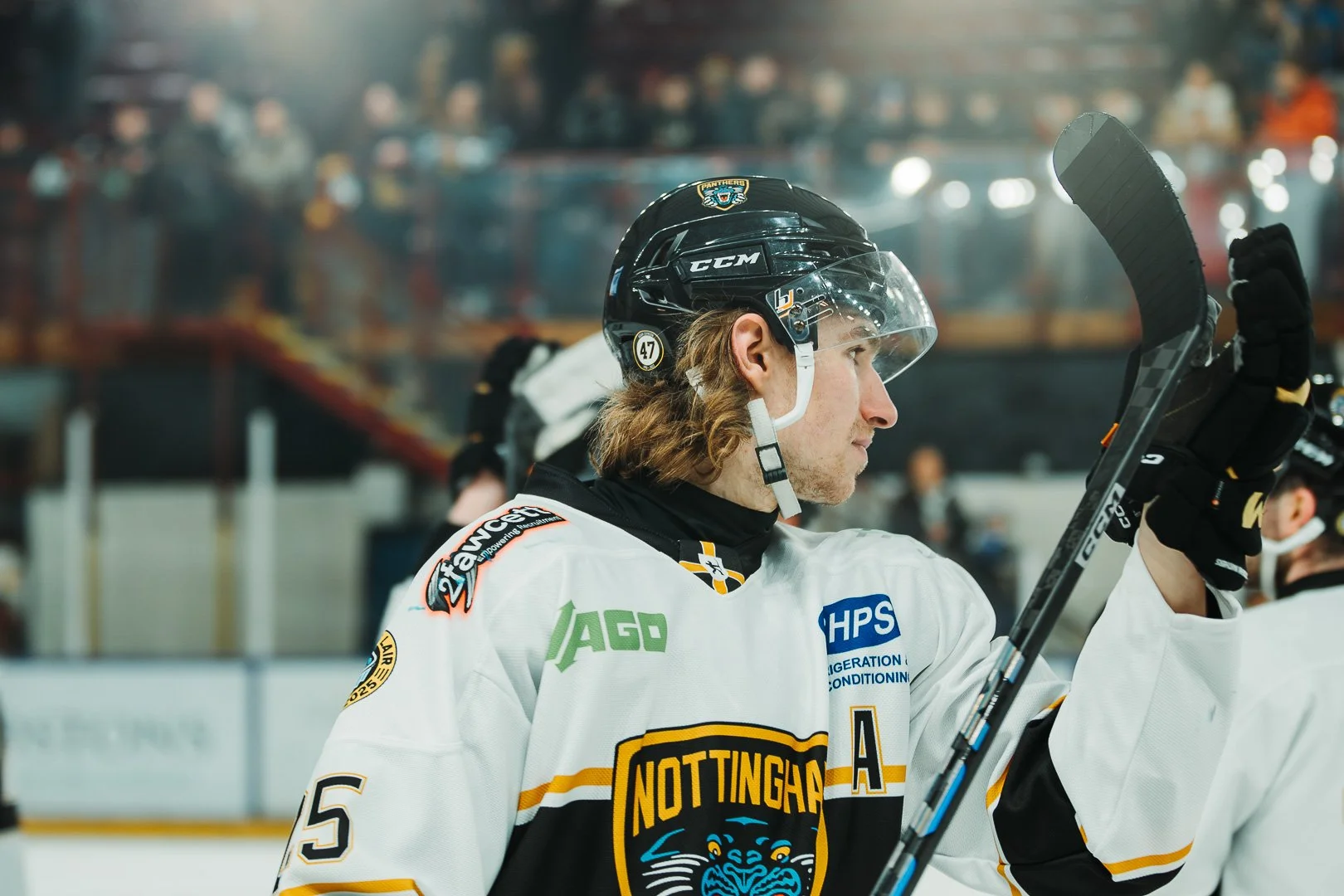 Ice hockey player in uniform raising his hand in a sports arena with spectators in the background.