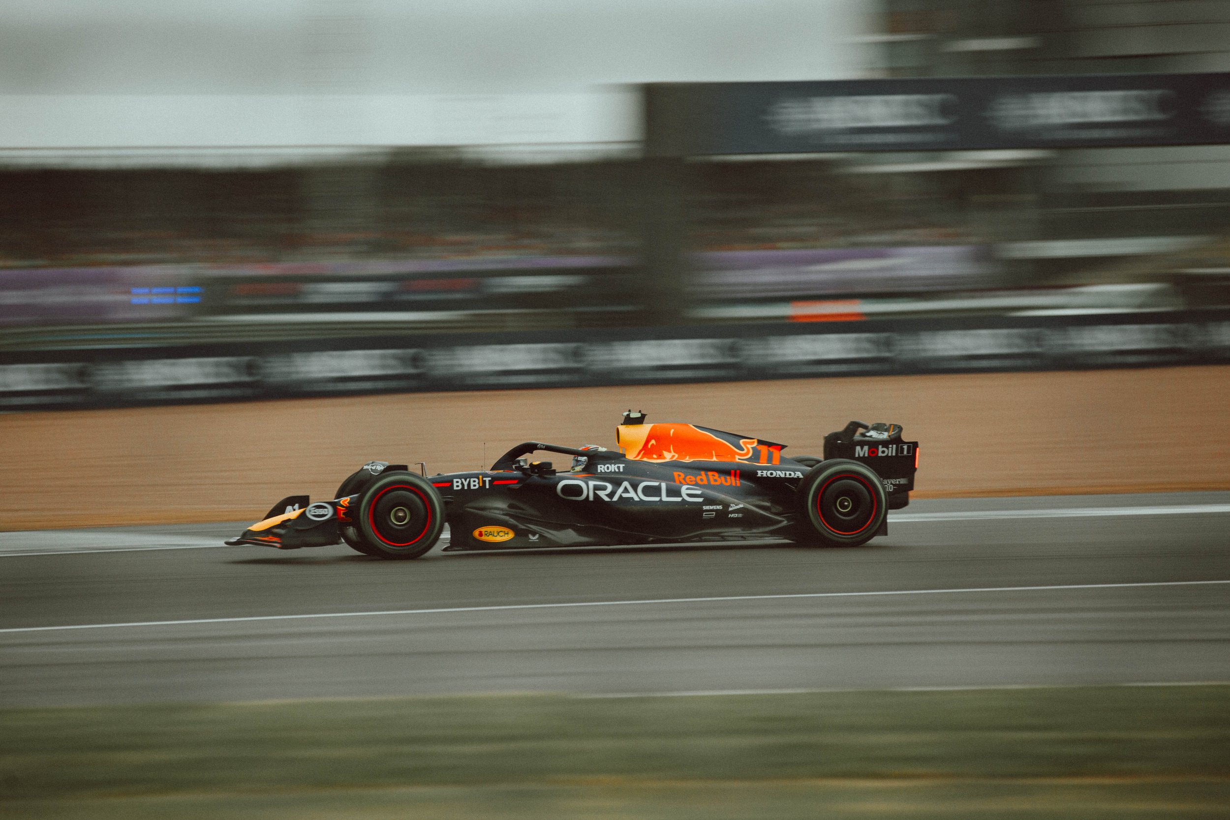 A Formula 1 race car speeding on a racetrack, with a livery featuring the Red Bull logo and sponsorships like Oracle and Honda.
