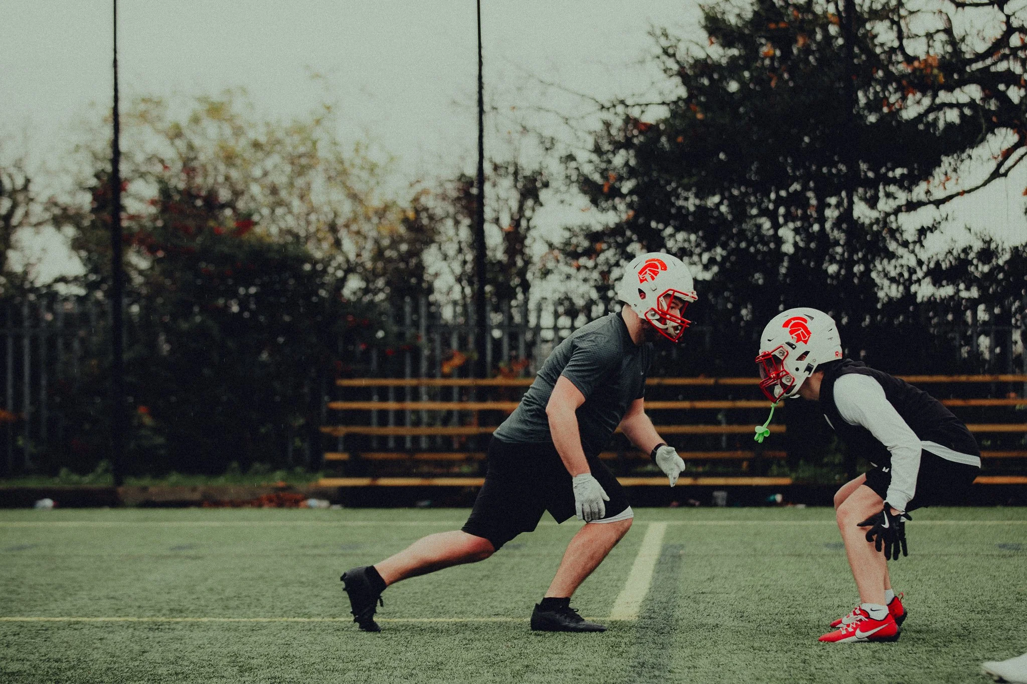 Two football players in helmets and gloves positioned on a field, preparing for a drill or practice session.