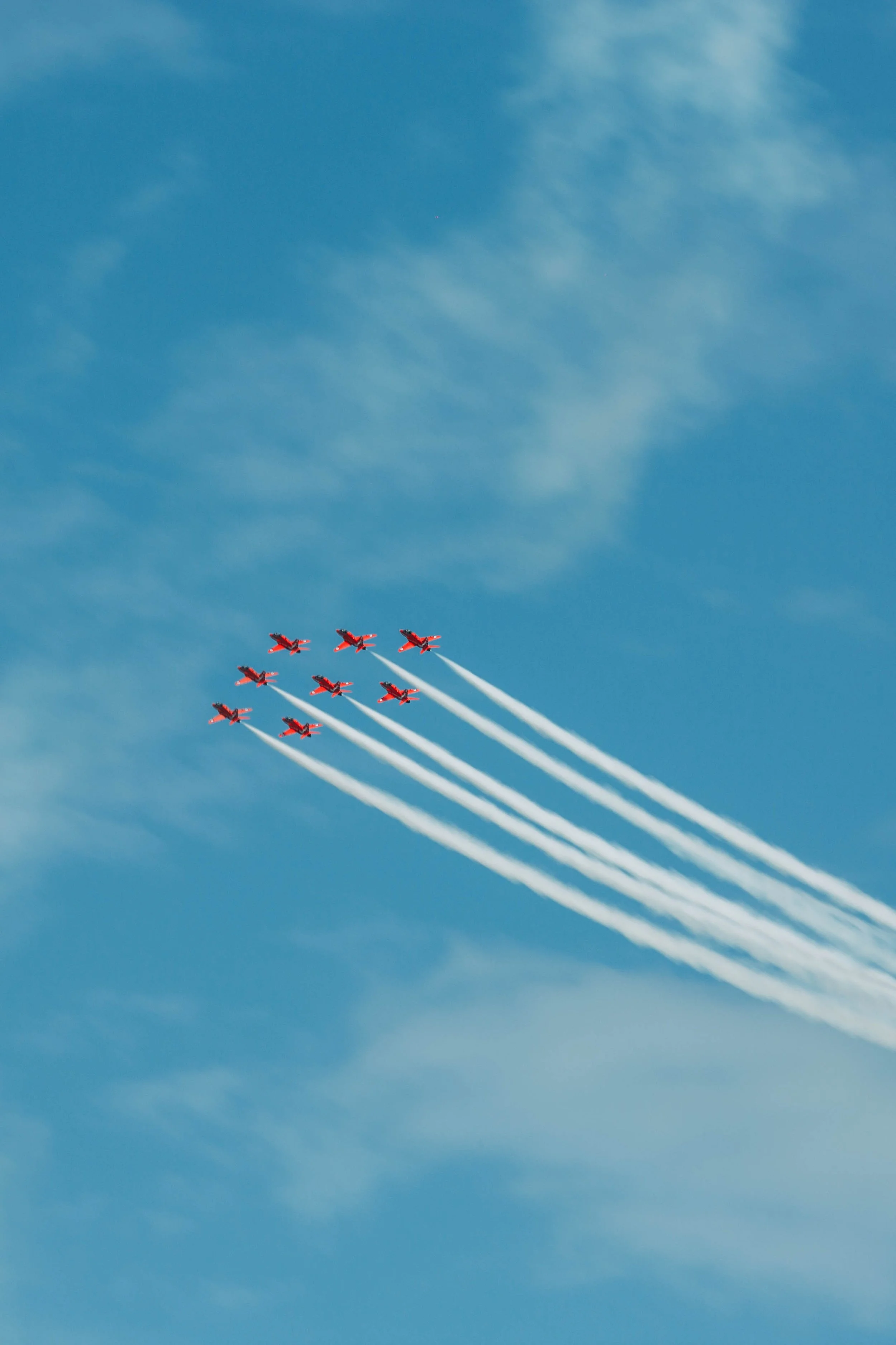 Aerial display by nine red airplanes soaring through the blue sky with white smoke trails.