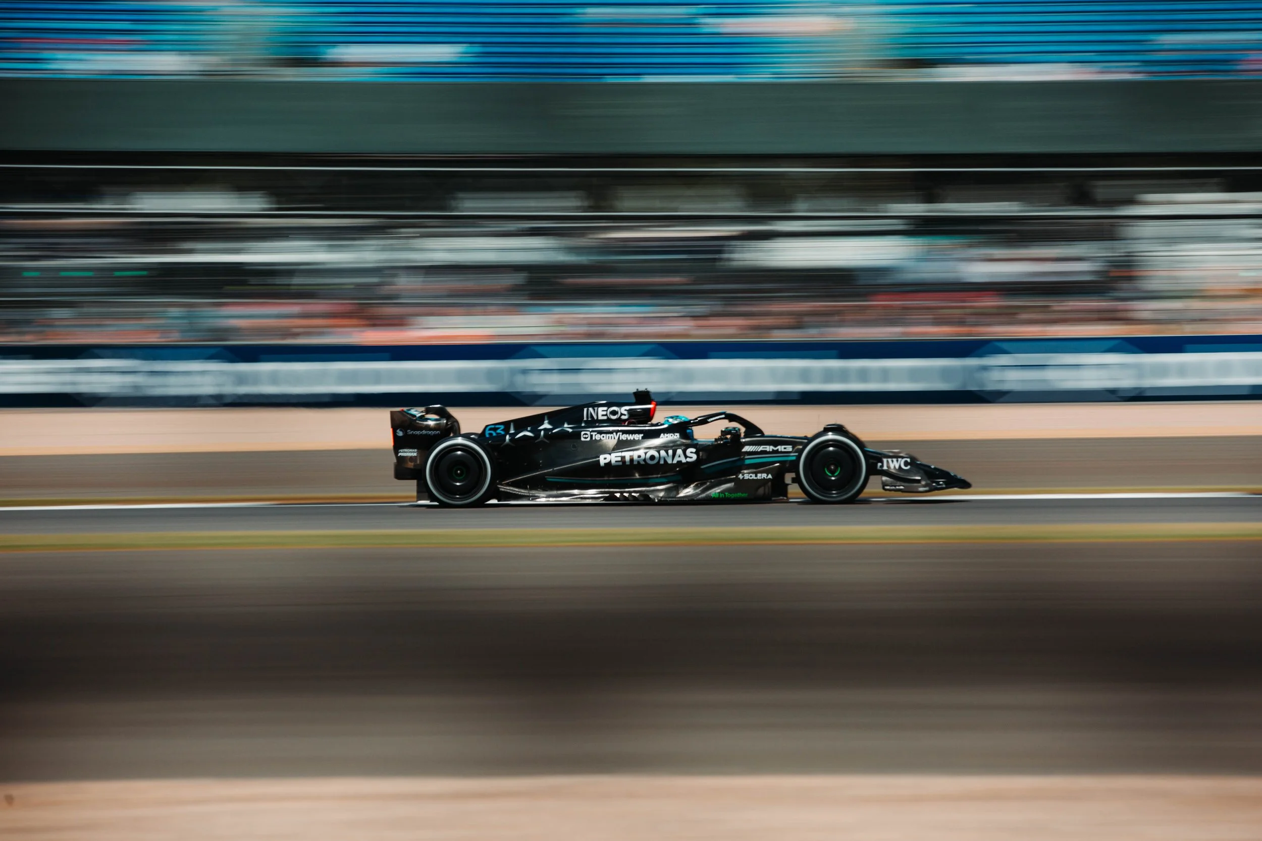 A black Formula 1 race car speeding along a race track during a race, with blurred background indicating high speed.