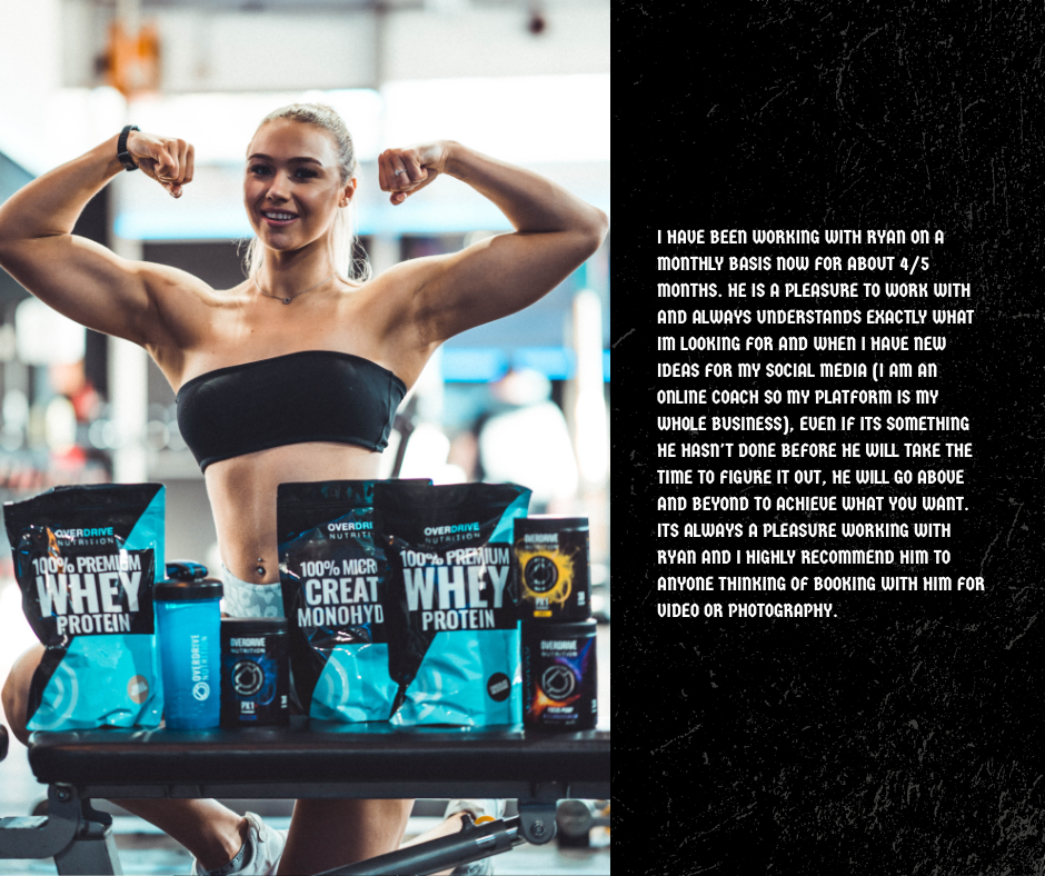A woman with blonde hair in a ponytail, wearing a black sports bra, flexing her arms at the gym, surrounded by containers of whey protein and supplements on a table.