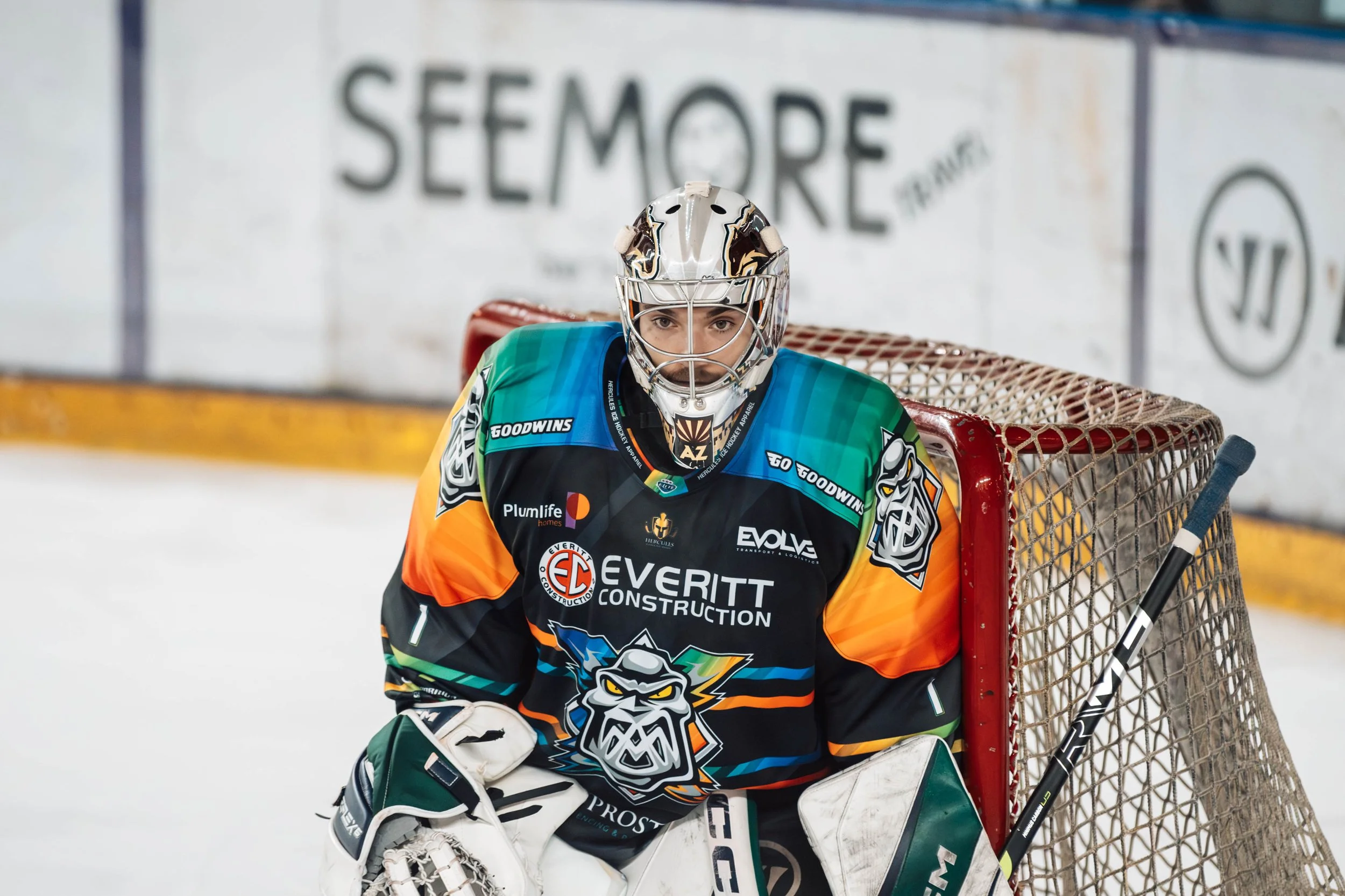 Hockey goalie in team jersey and helmet standing in front of the net during a game.
