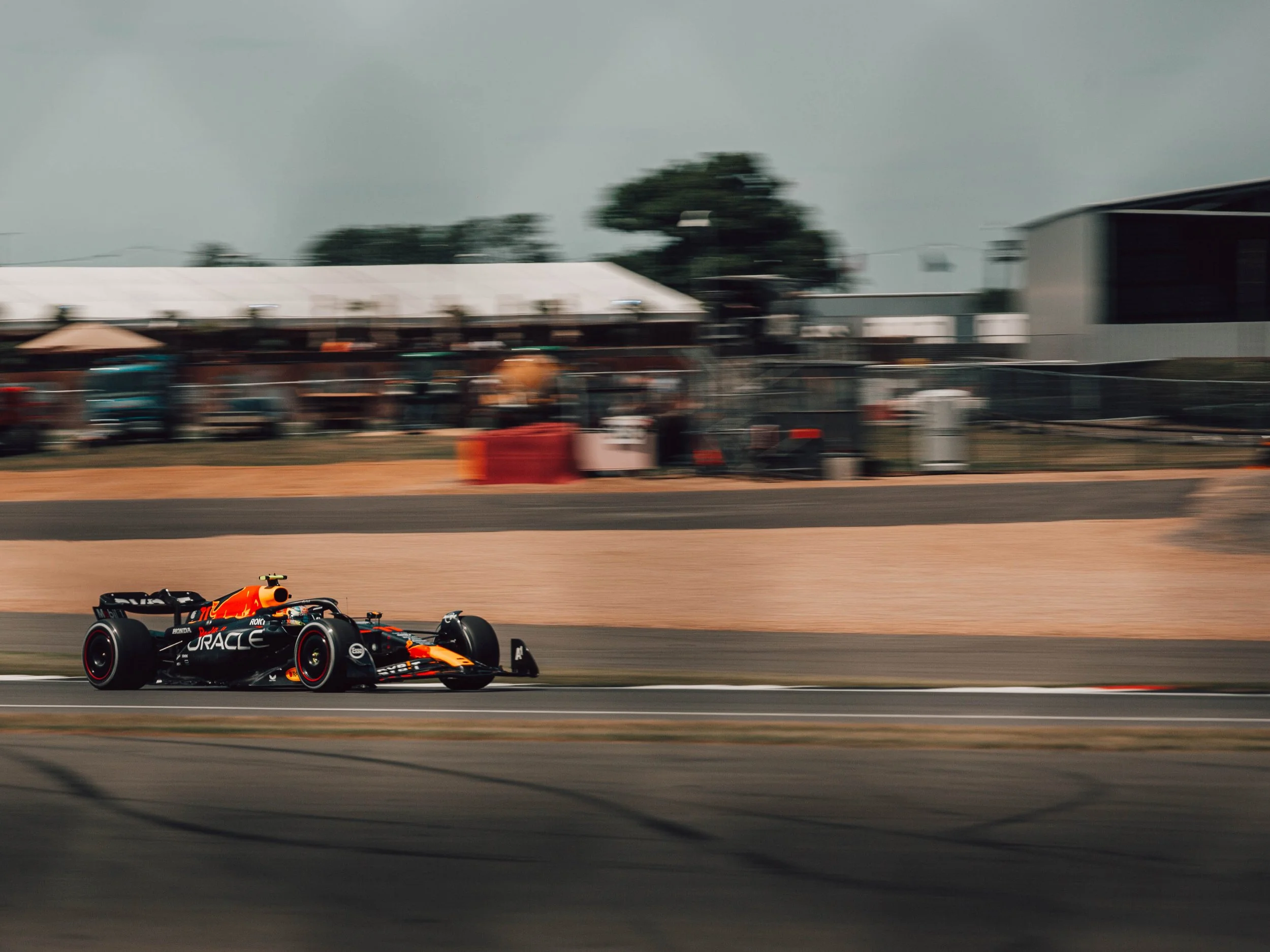 A Formula 1 race car on a racetrack during a race or practice, with a blurred background of spectators and structures.