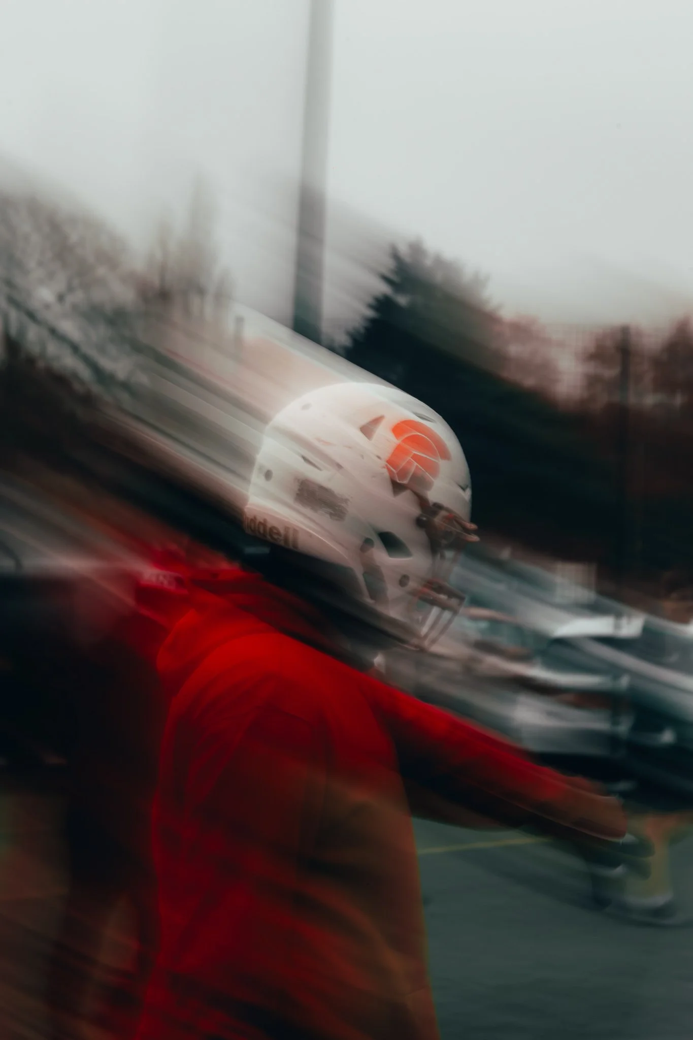 A person wearing a helmet and orange jacket standing on a railway track with a train moving past, creating a motion blur effect.