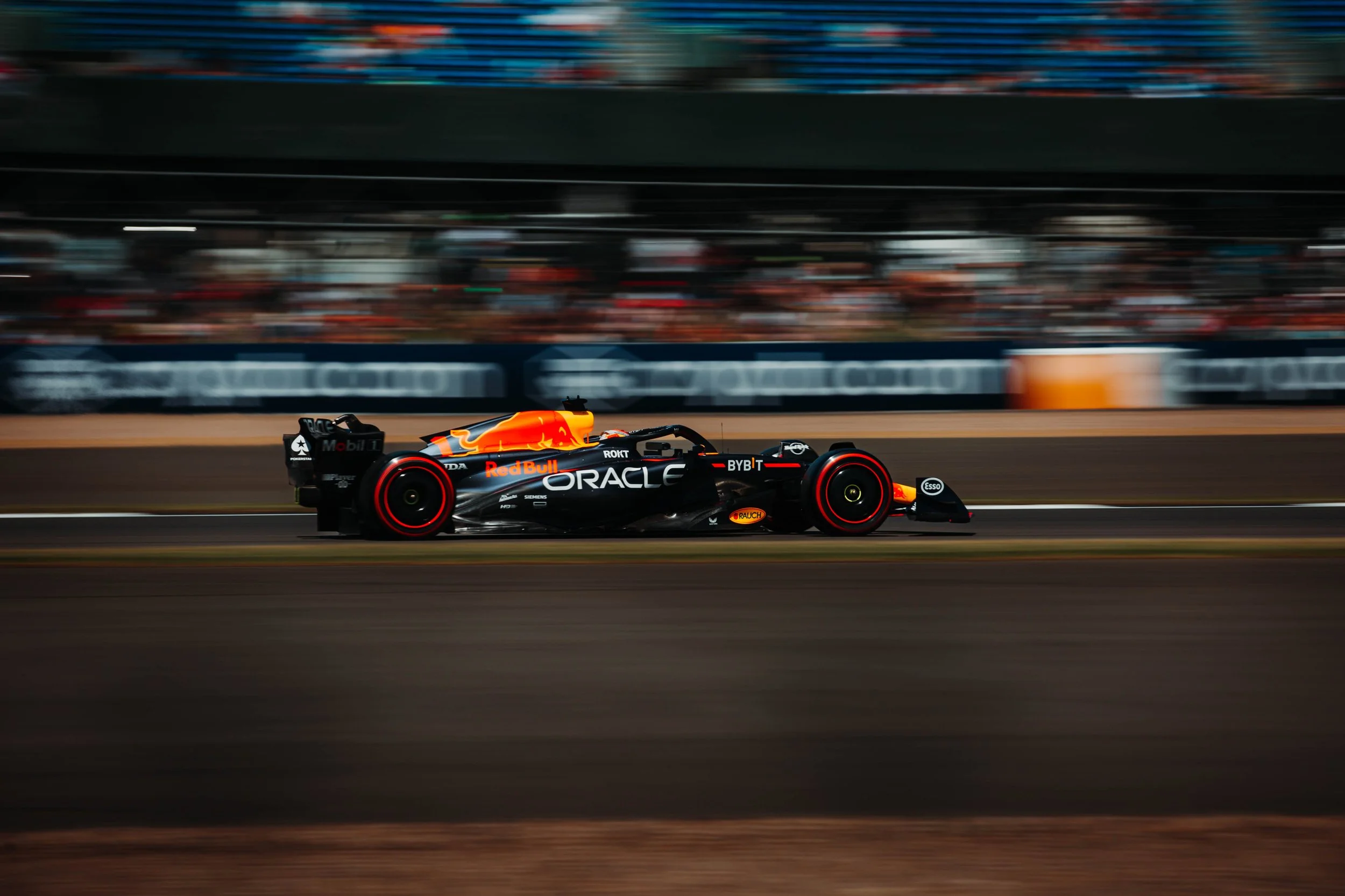 A black Formula 1 race car with Red Bull branding speeding on a race track, with motion blur in the background.