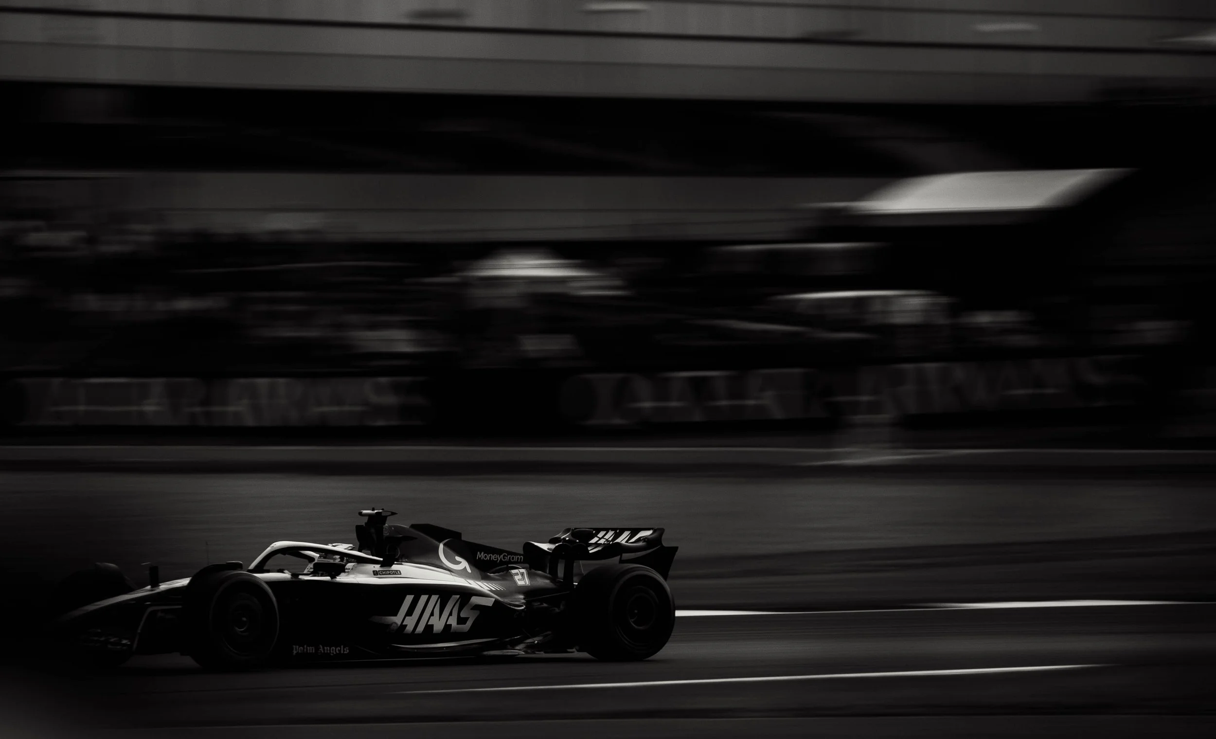 A black and white photo of a race car on a track with a blurred grandstand in the background.