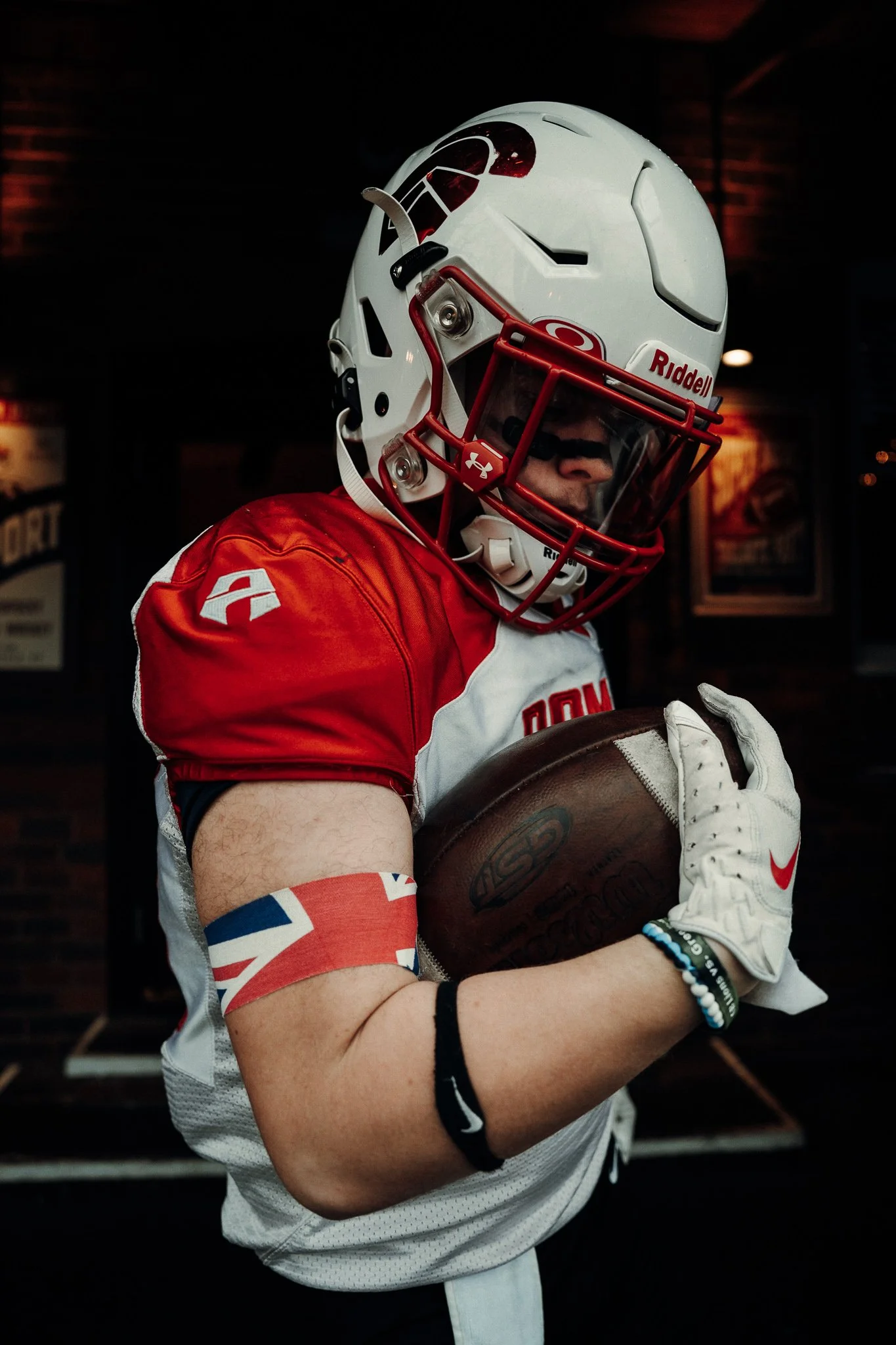 American football player wearing a helmet and uniform holding a football indoors.