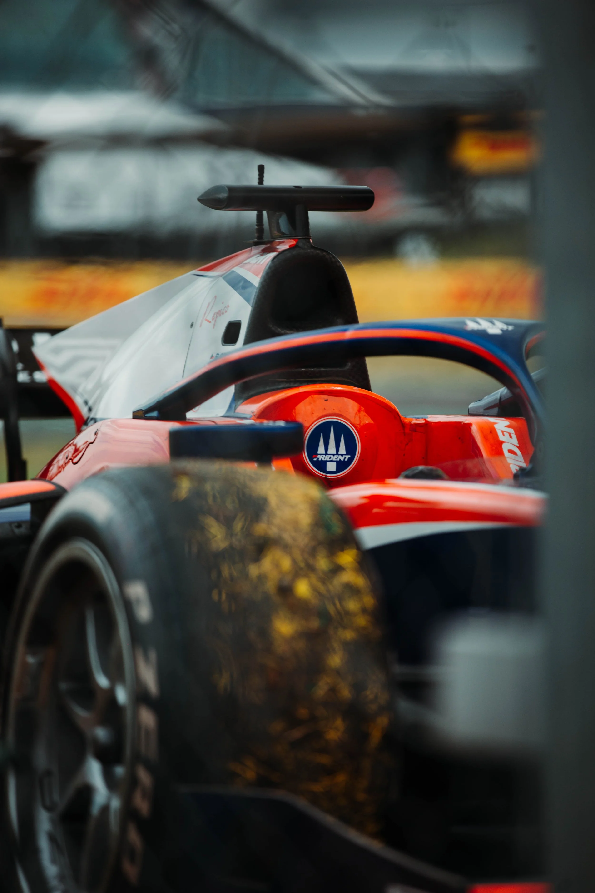 Close-up view of a red and white racing car with a focus on the front wheel, partially surrounded by a metal frame, with the cockpit and a rear wing visible in the background.