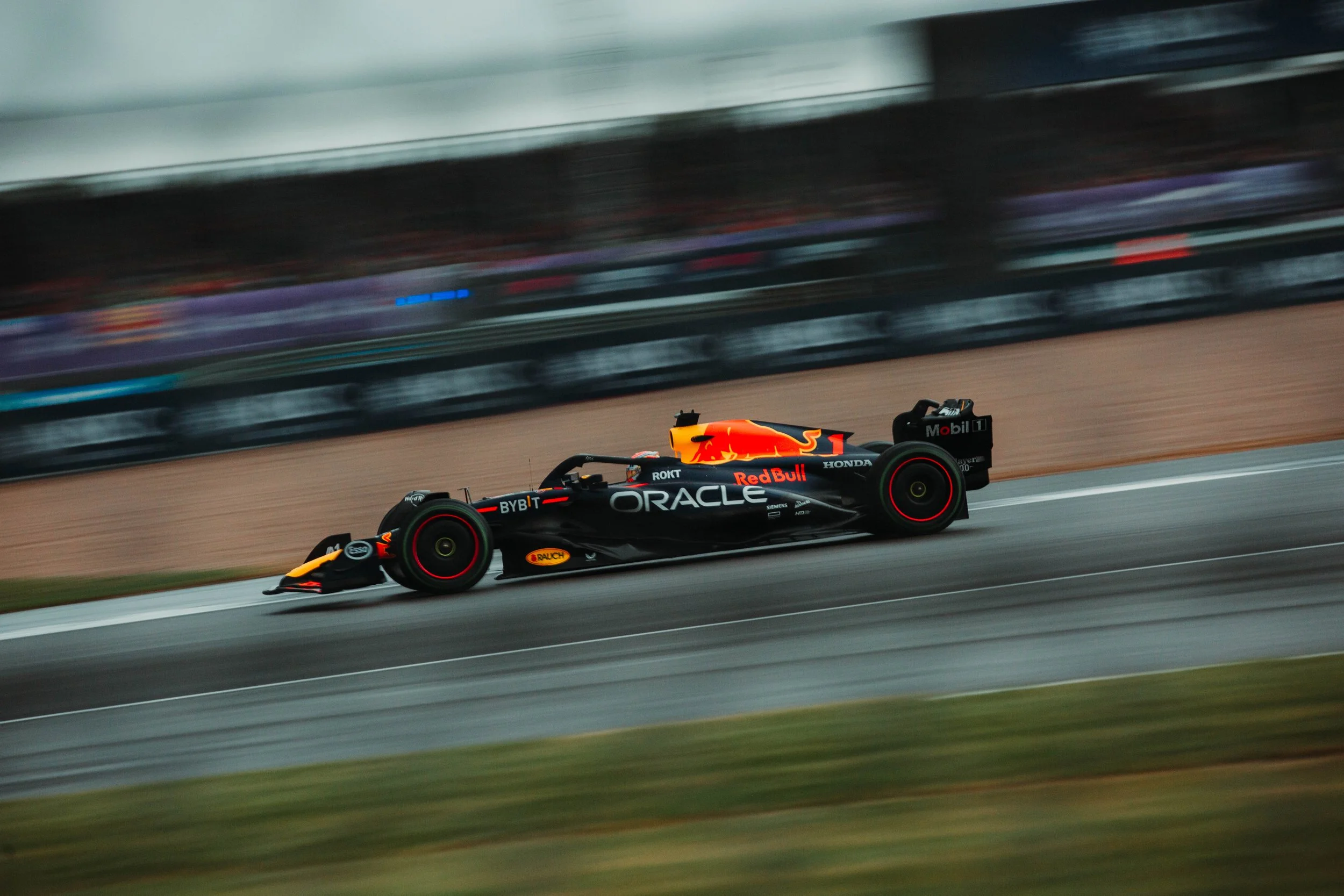 A race car on a racetrack with sponsors and branding, including Oracle and Red Bull, moving quickly with motion blur in the background.