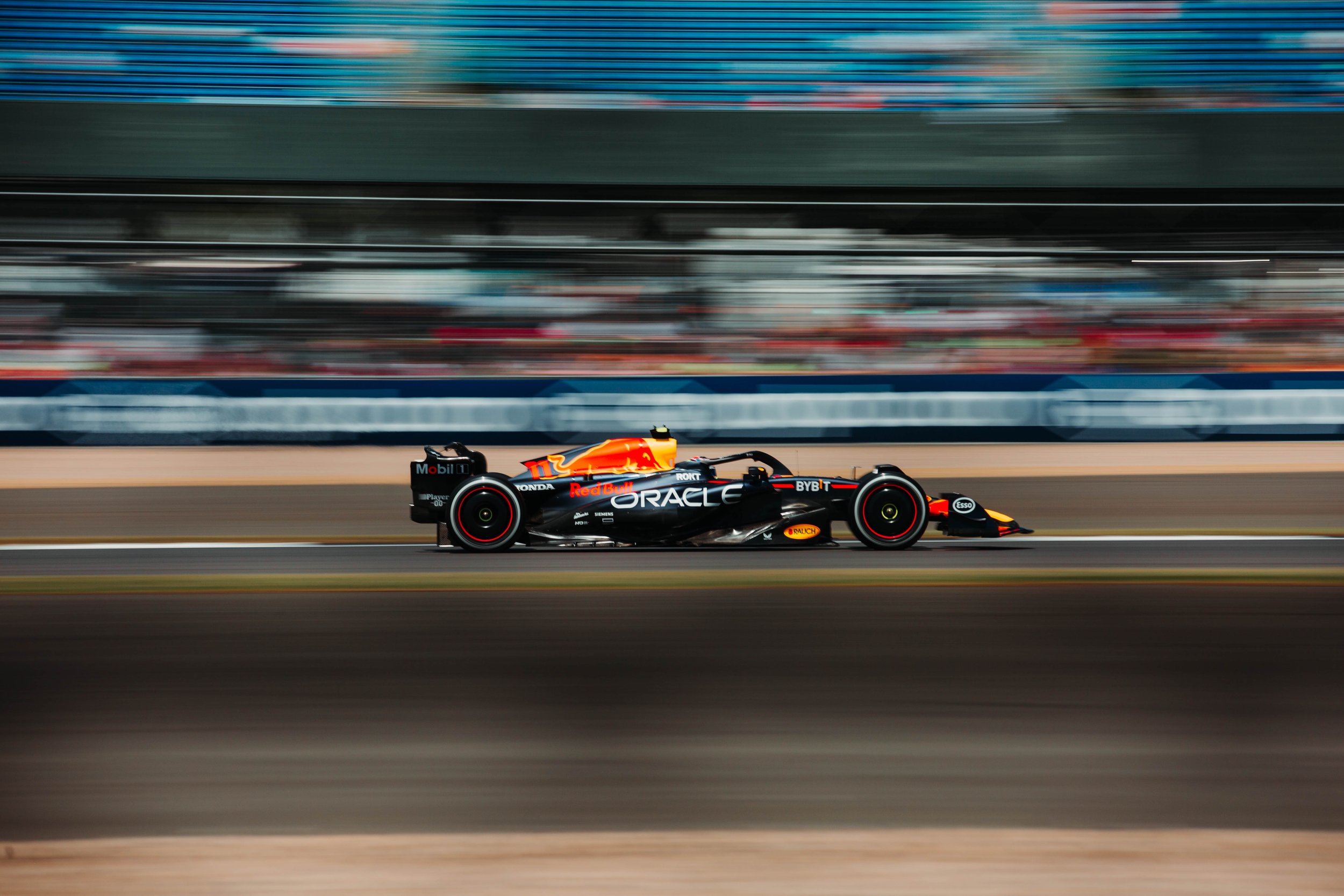A Formula 1 race car on the track during a race, with sponsorship logos visible, including Oracle and Red Bull.
