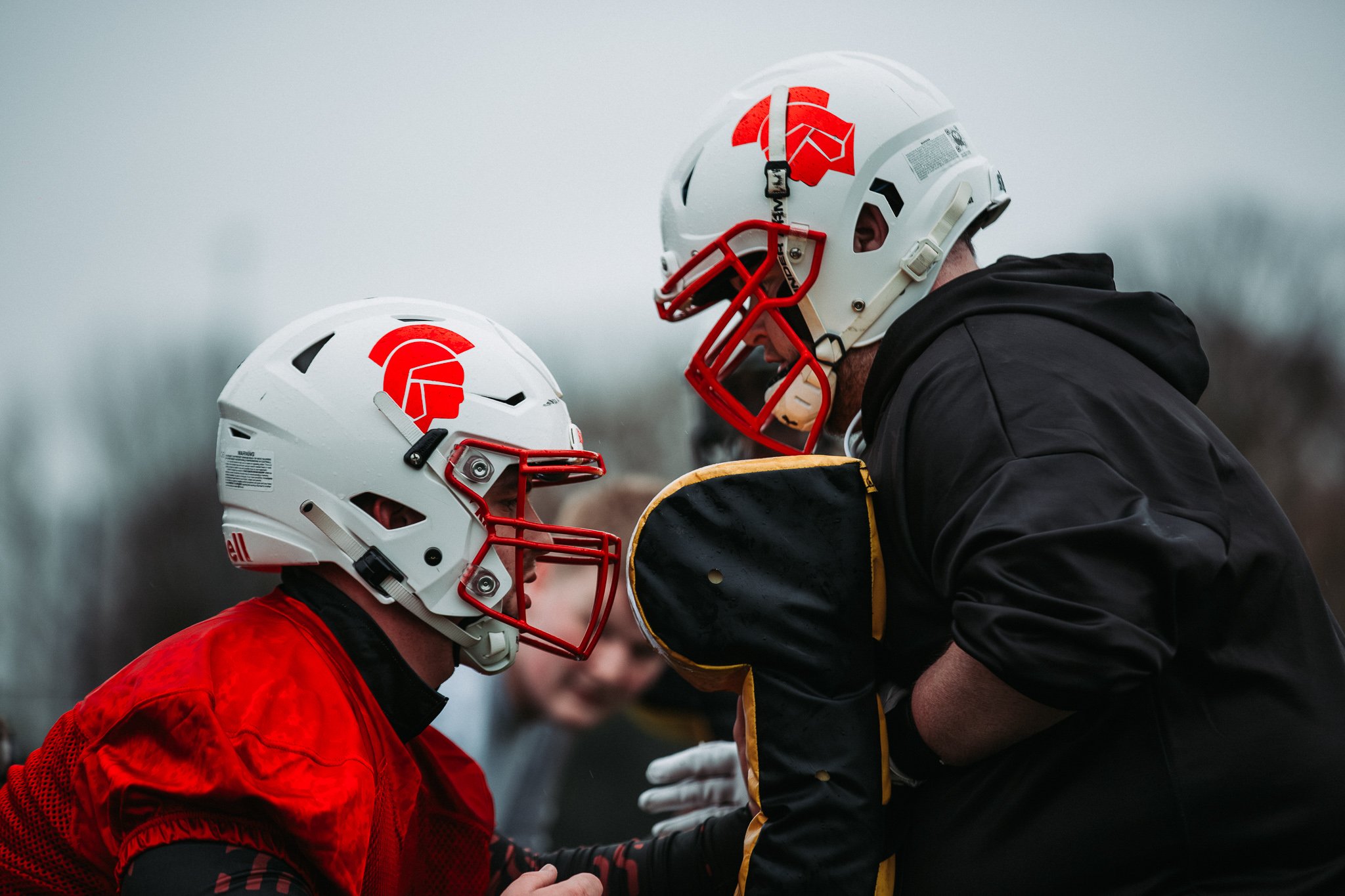 Two American football players in helmets and uniforms facing each other, with one appearing to give instructions or encouragement to the other.