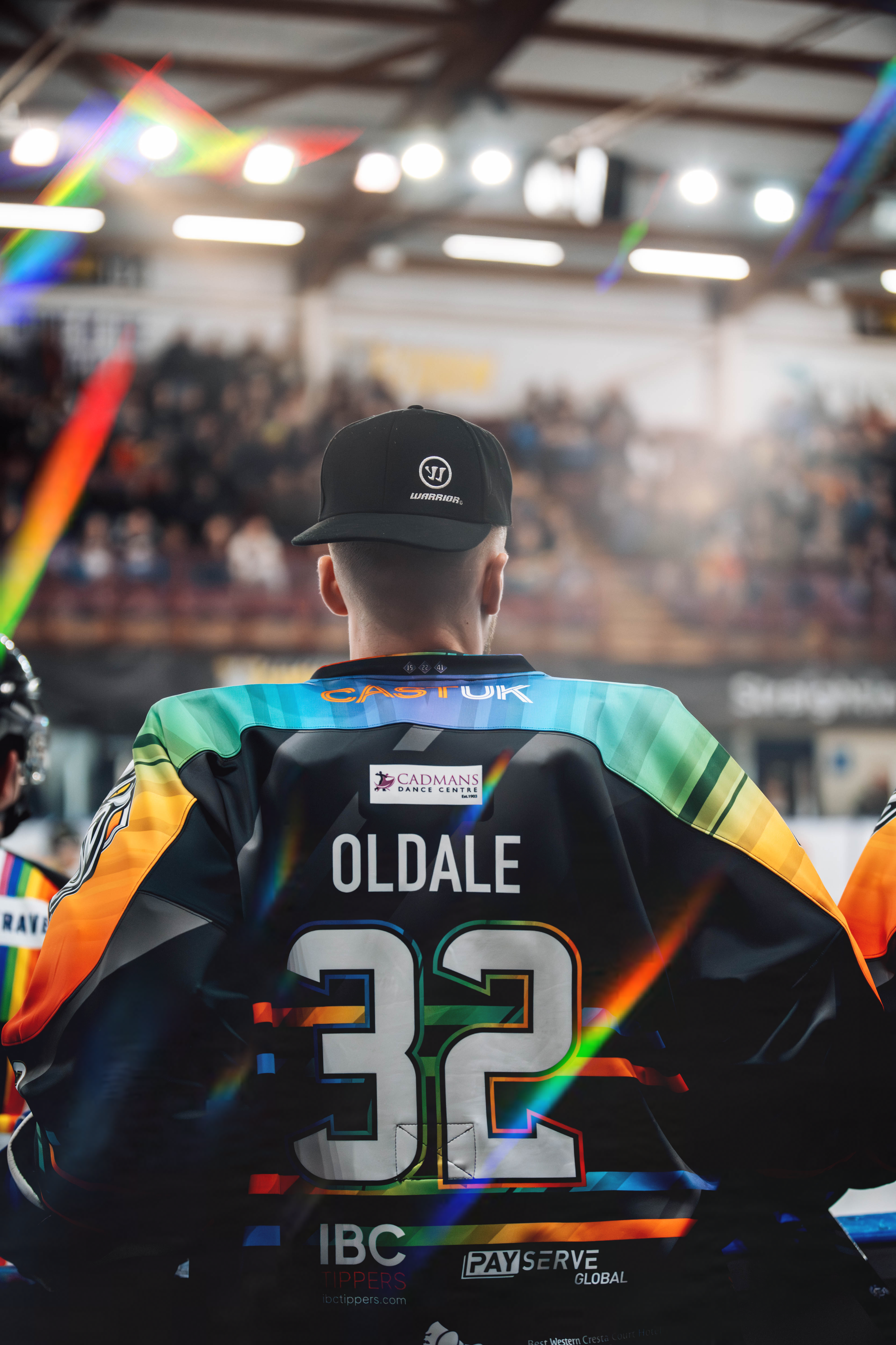 A hockey player in a colorful jersey with the name 'Oldale' and number 32 on the back, standing in an indoor arena with fans in the background.