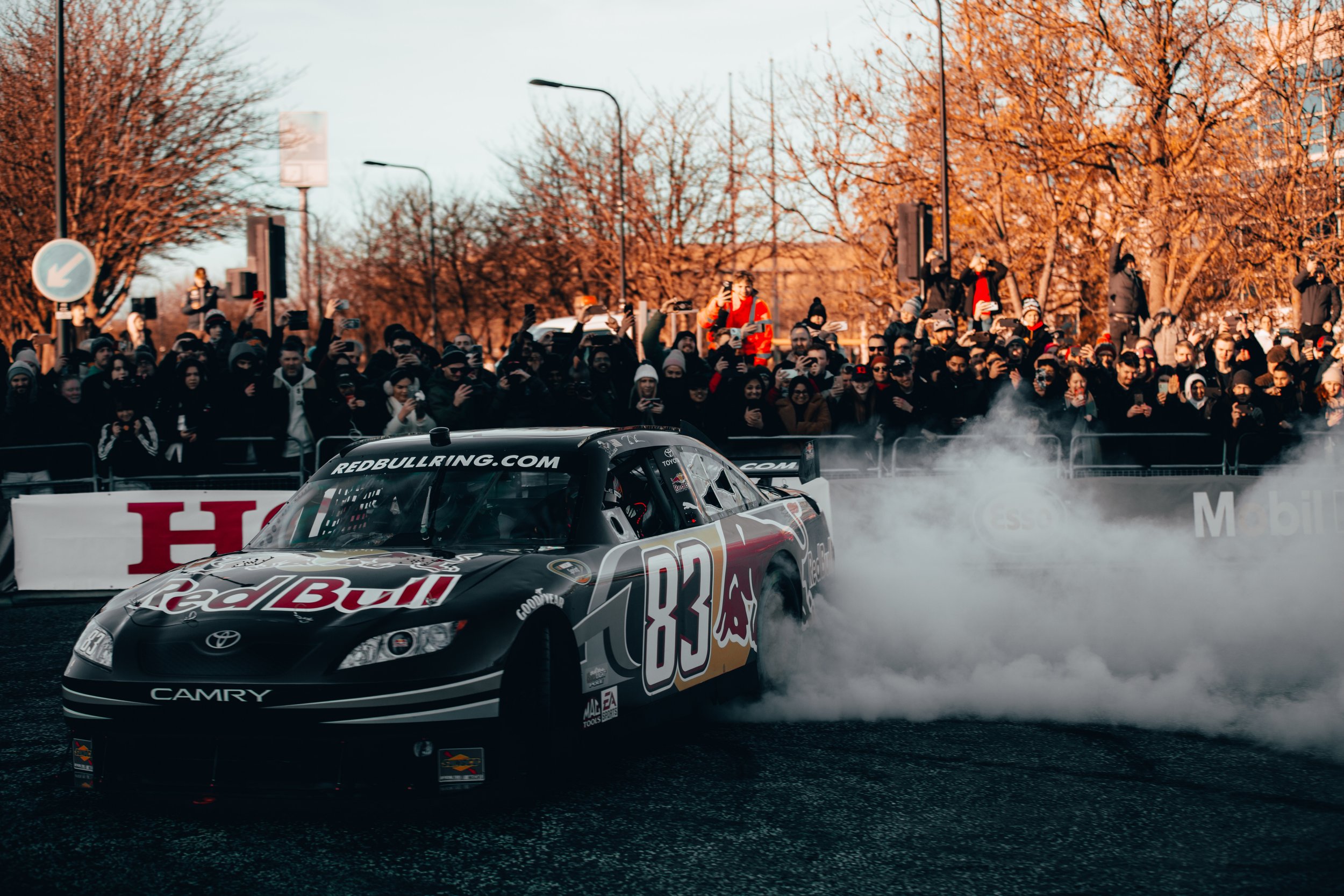 A racing car doing a burnout on the track while a crowd watches from the sidelines.