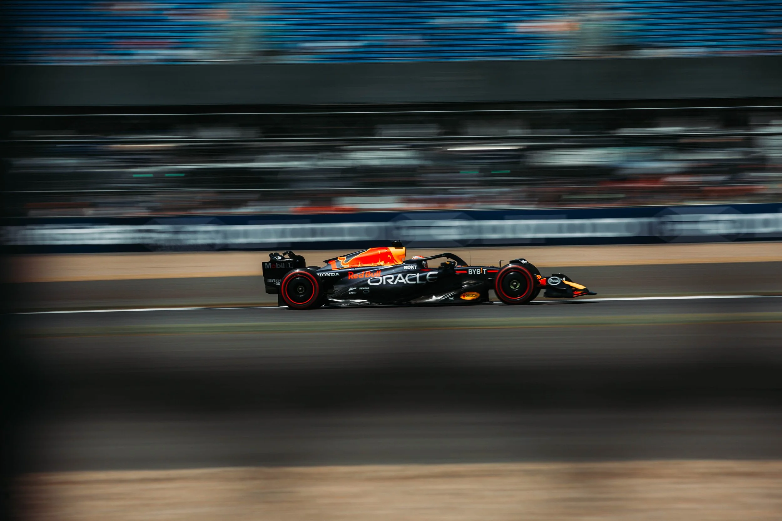 A Formula 1 race car speeding along a racetrack, branded with sponsors including Oracle and Red Bull, with a blurred background indicating high speed.