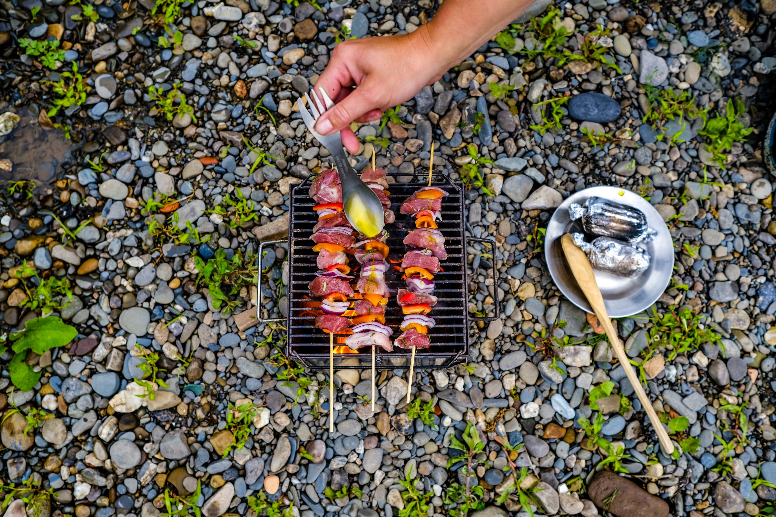 meat and vegetable kebabs being cooked on a griddle with oil being poured over them