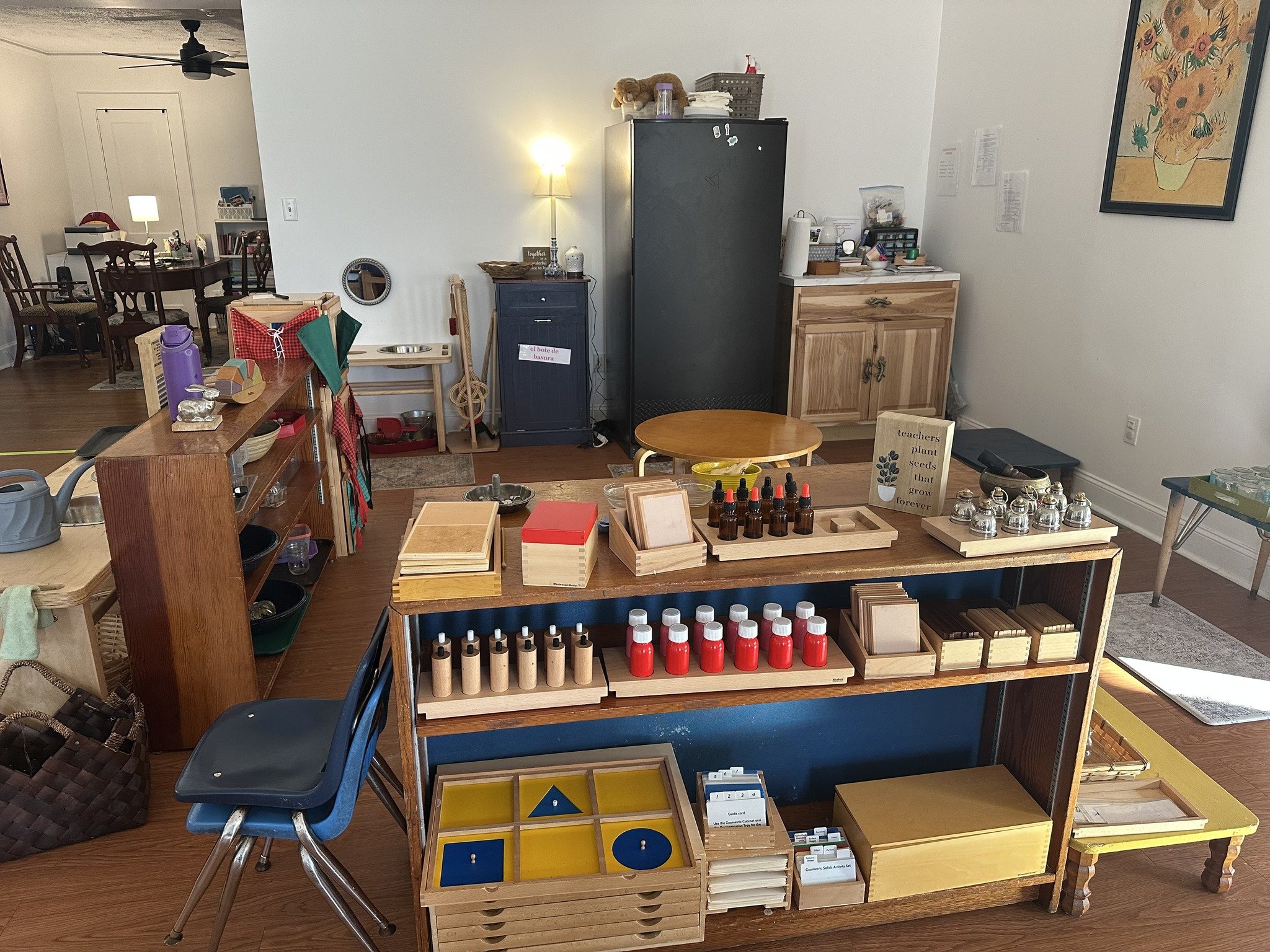 Interior of a classroom or therapy room with various educational and sensory materials on wooden shelves and tables, including bottles, blocks, and other learning toys.