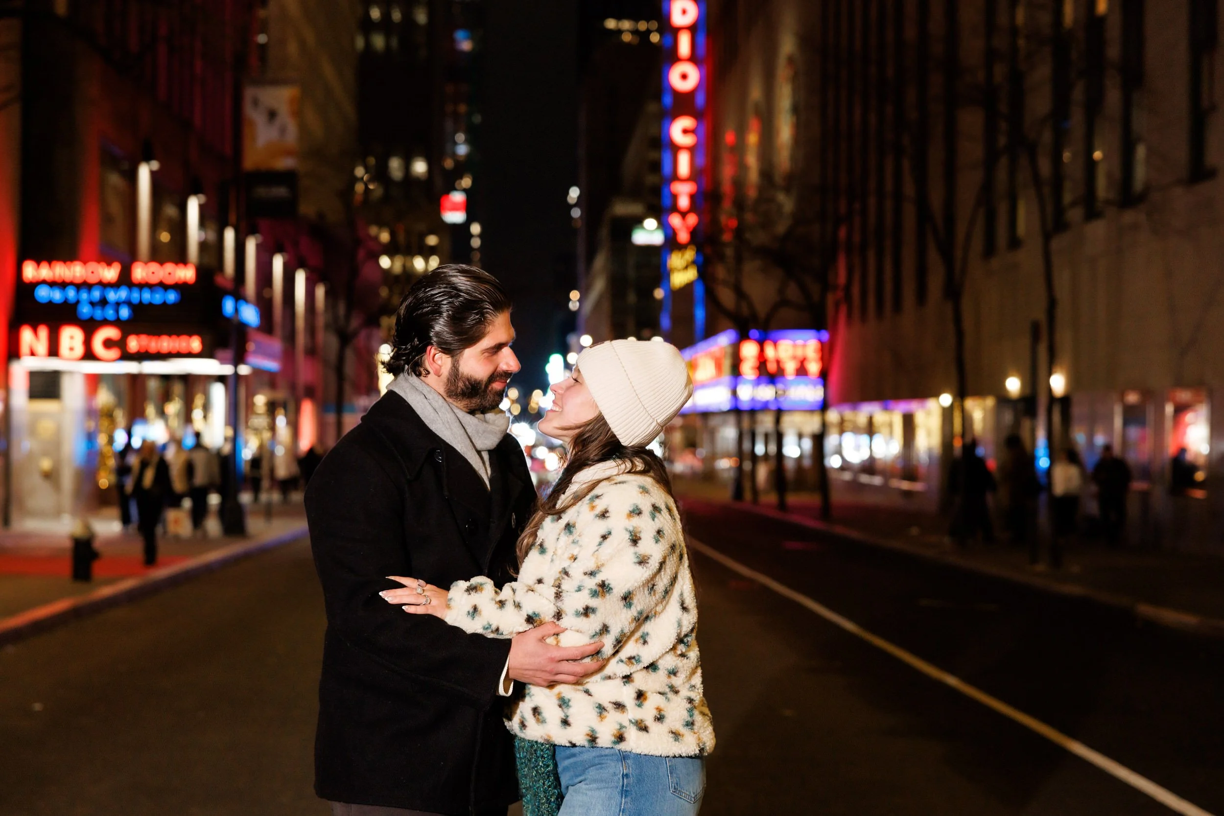 A couple standing in the middle of a city street with their arms around each other about to kiss at night 
