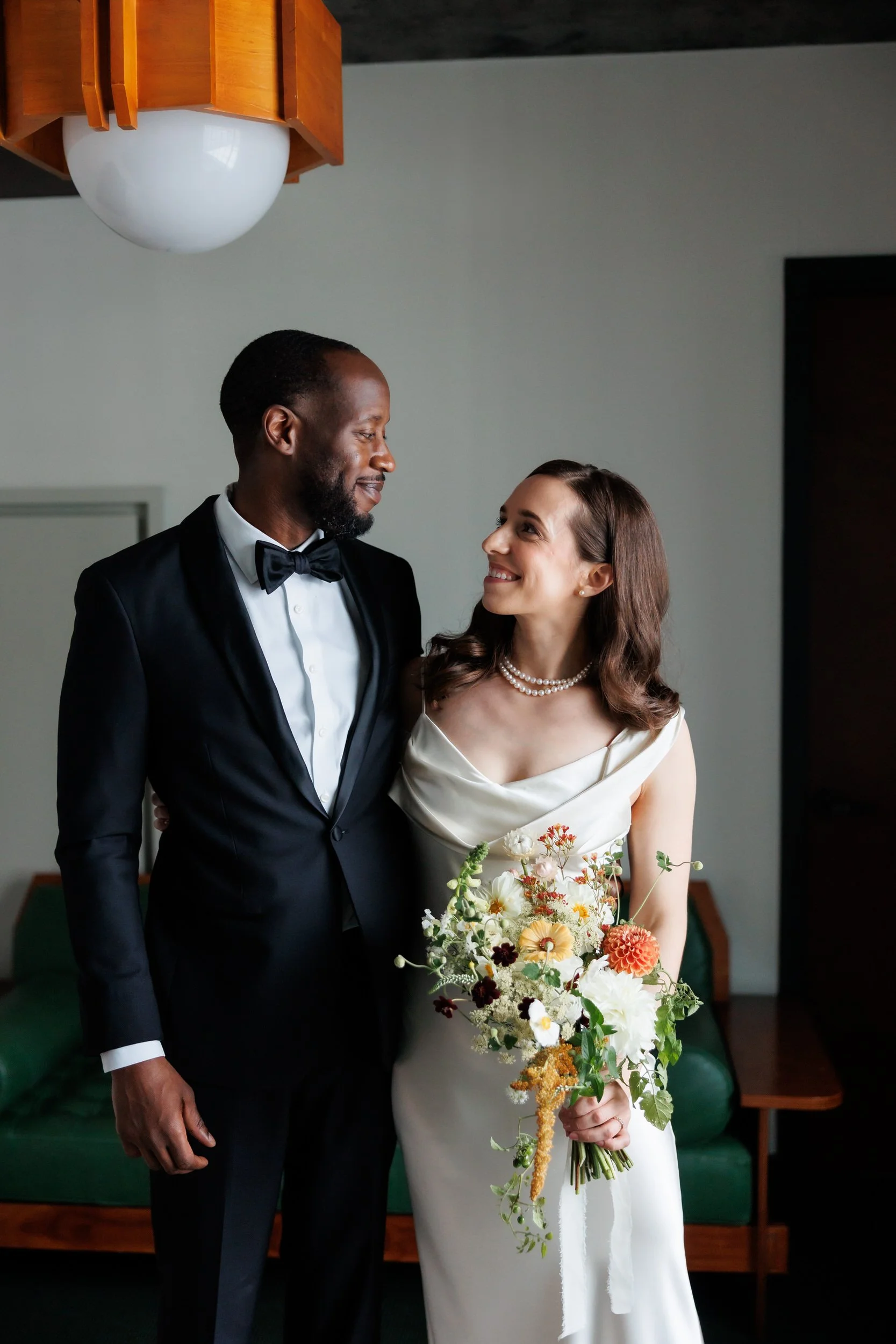 A newlywed couple smiling at each other as they have one arm wrapped around each other