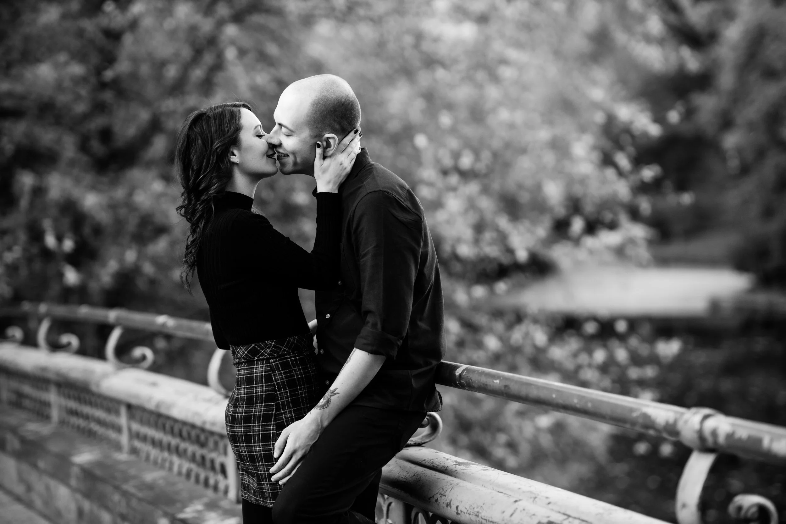 A couple kissing while leaning in the railing of a bridge