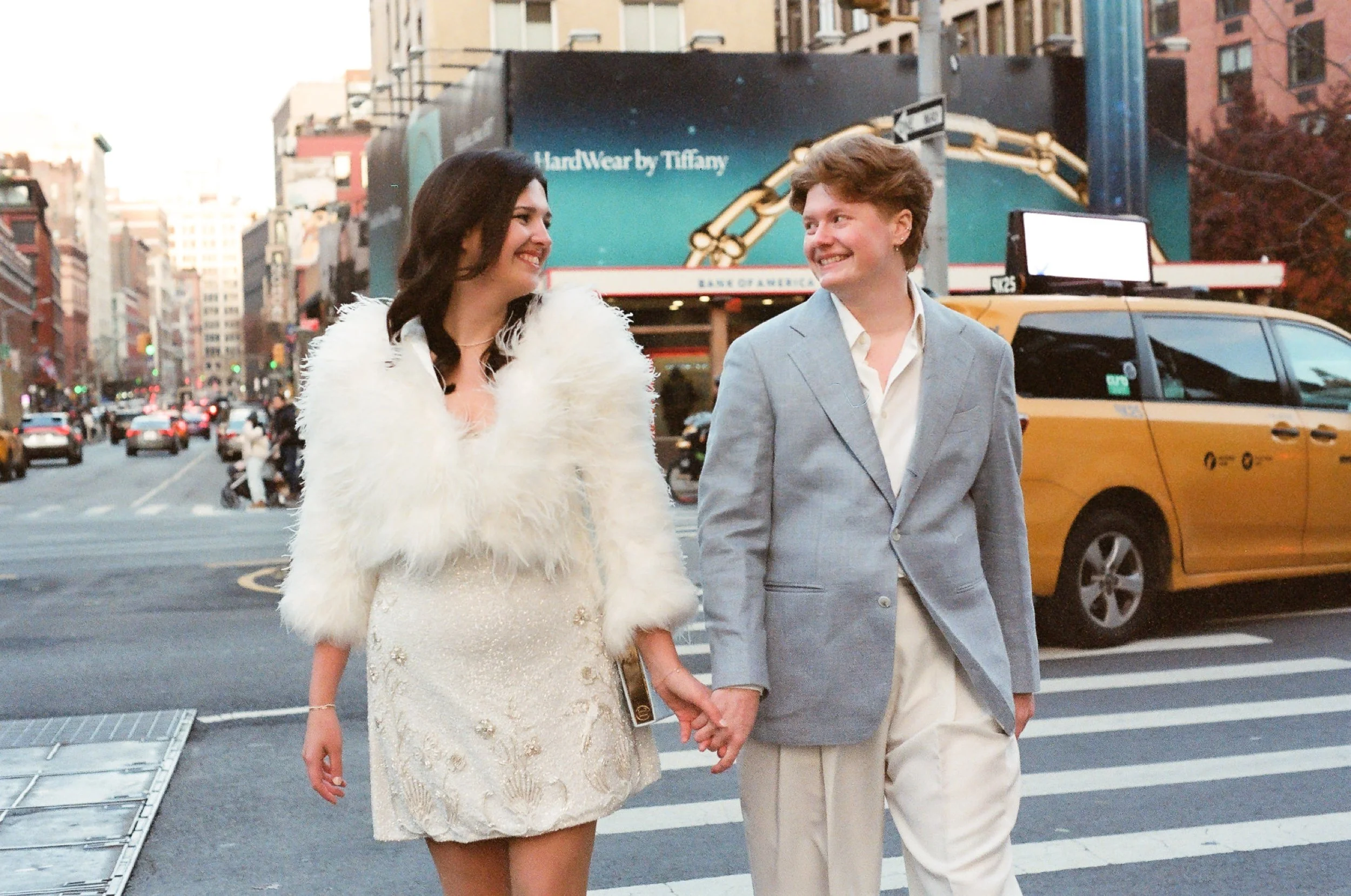 Couple holds hands and crosses the street in NYC in front of yellow cabs
