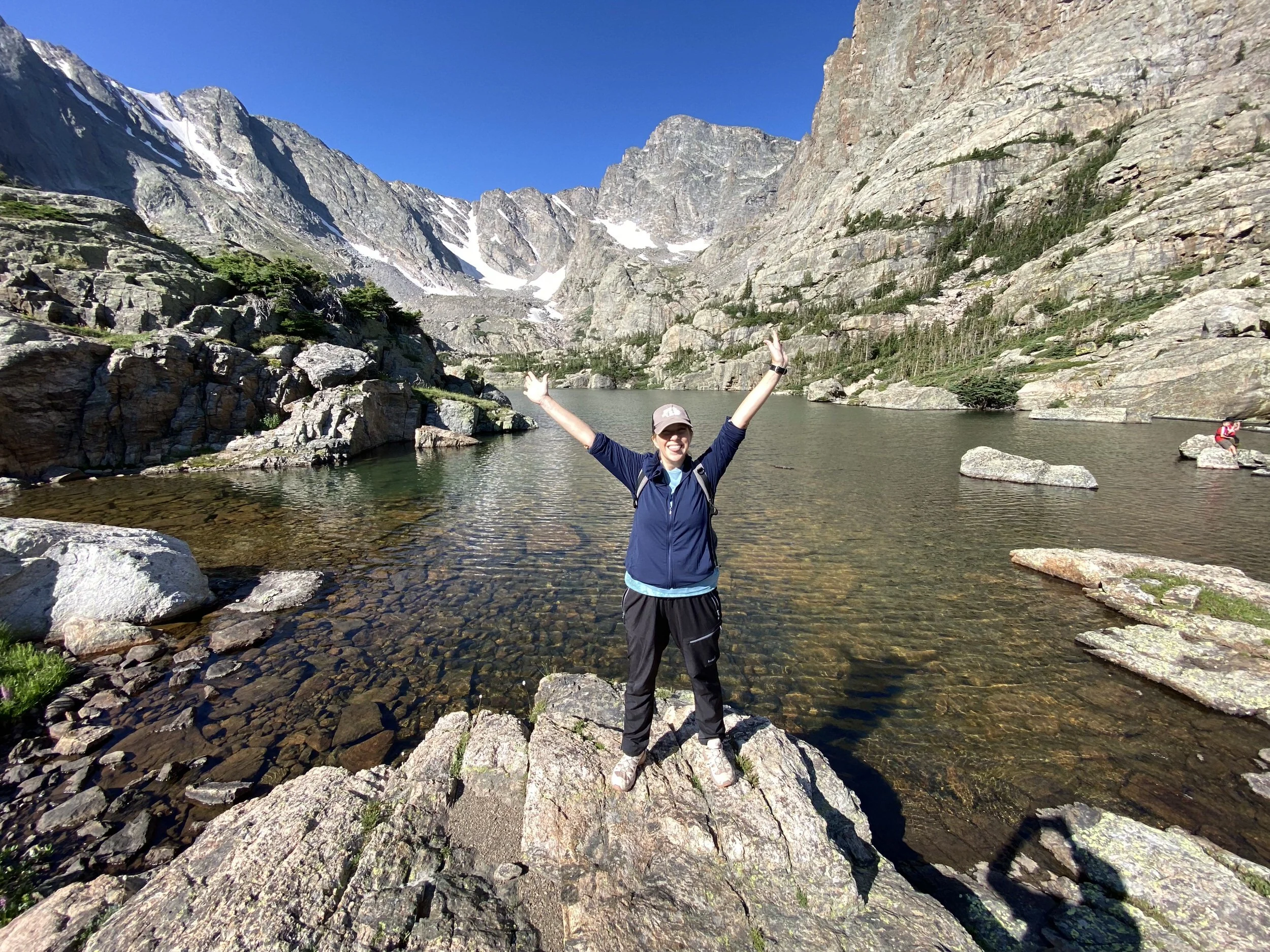 Sarah standing on a rock in front of an alpine lake with her arms outstretched