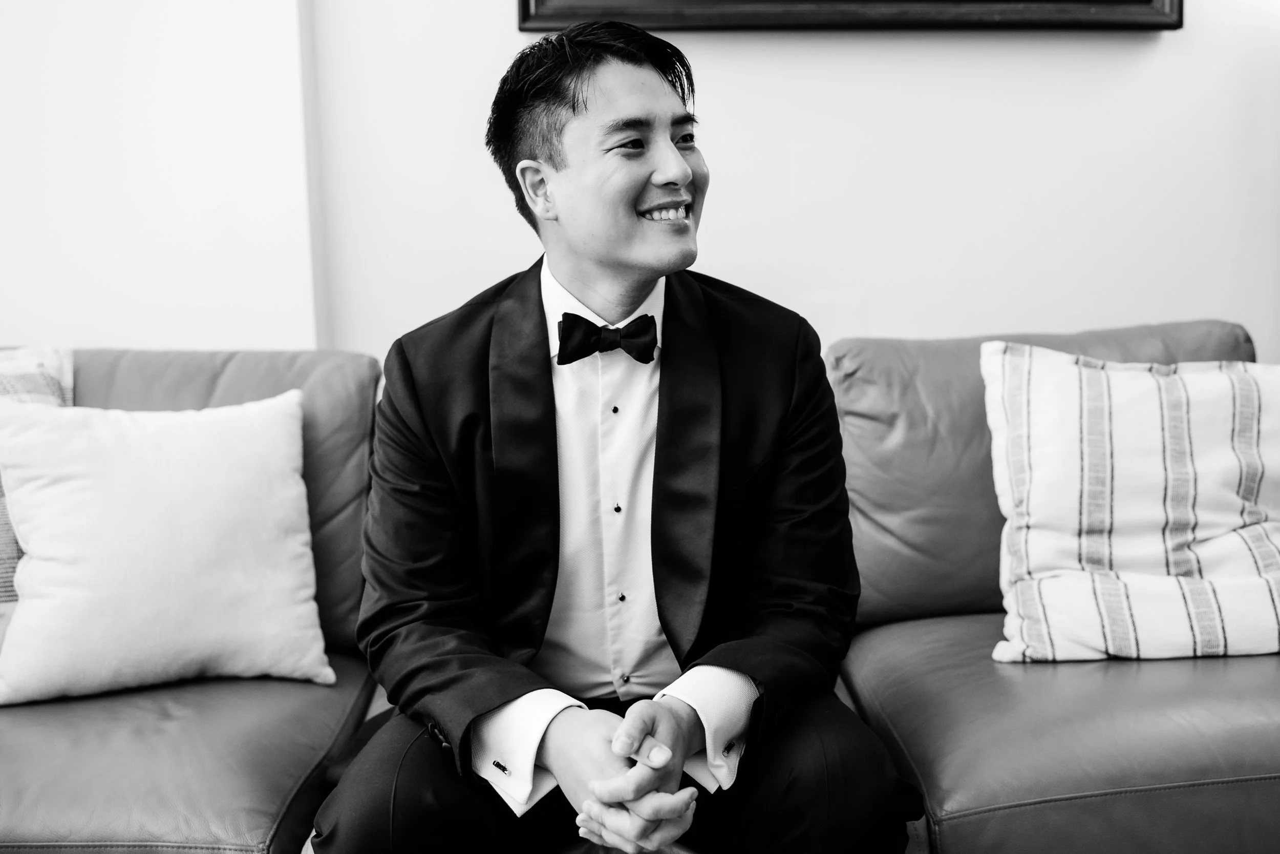  Groom sitting on couch and smiling after getting ready for wedding. 