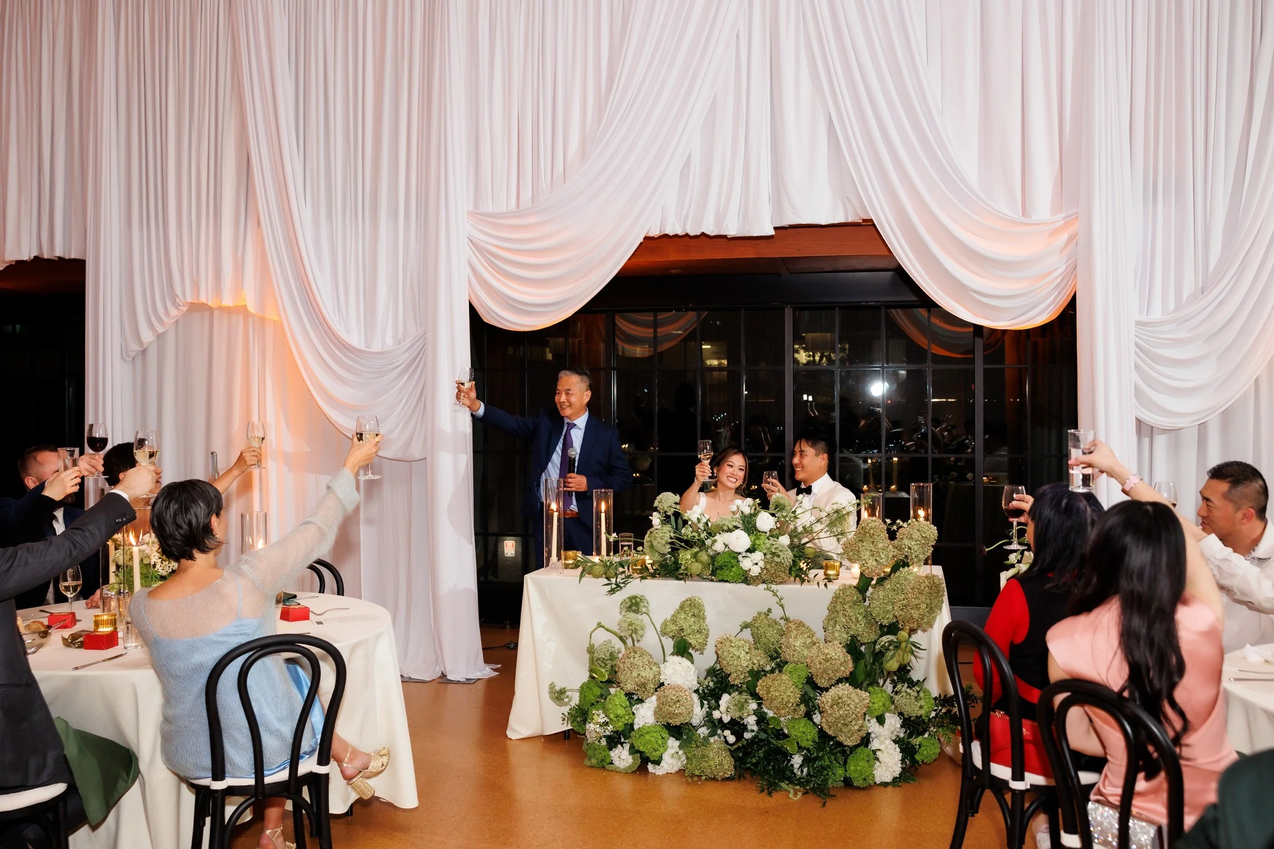  A couple and their guests raise their glasses in a toast during a wedding reception 