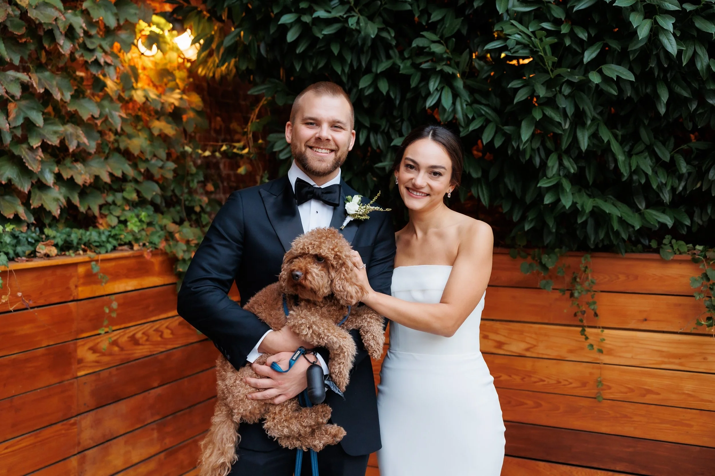  Couple poses with their dog that is dressed in a wedding tux 