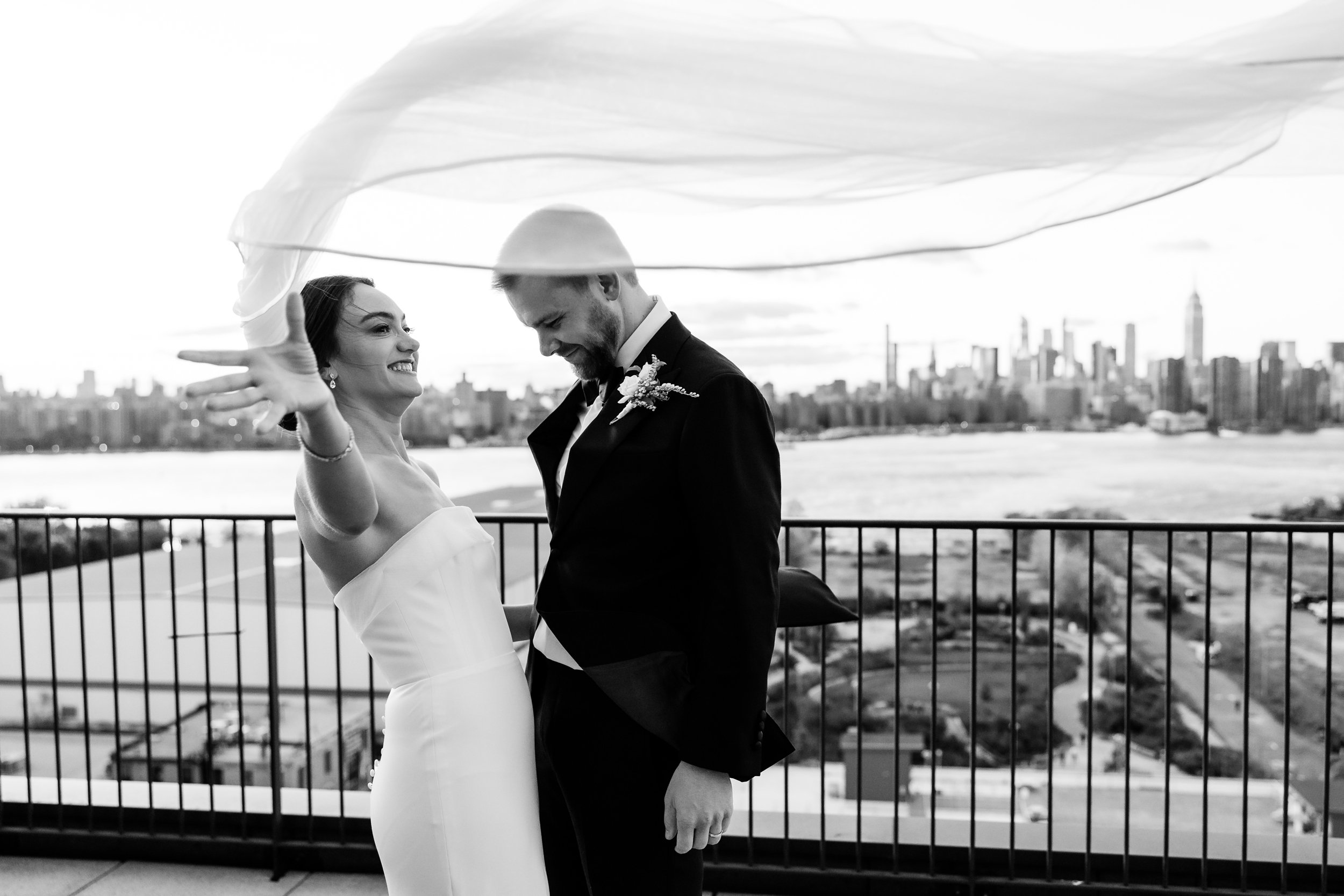  Bride and groom on balcony overlooking NYC skyline and bride tries to catch veil that is blowing away 