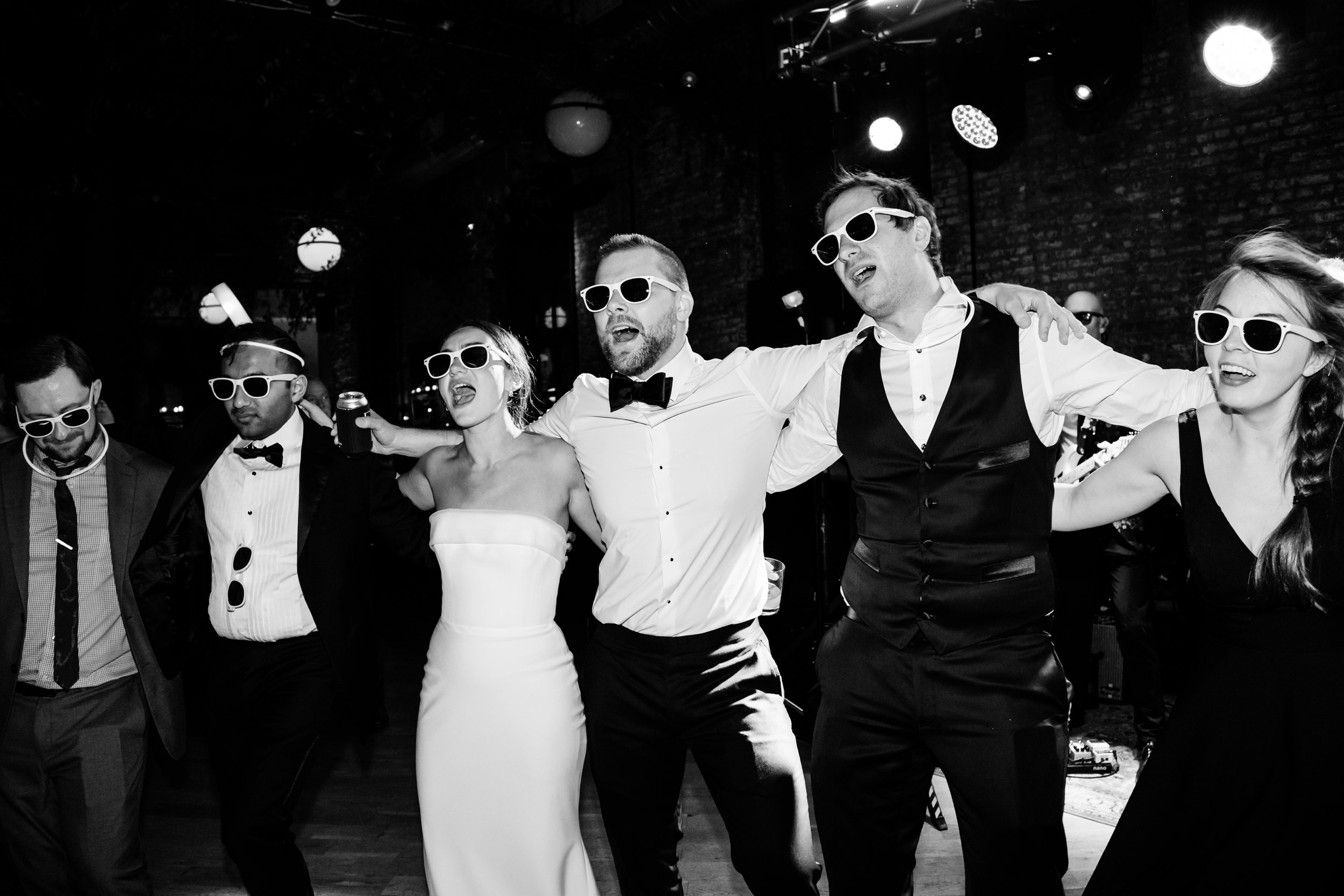  wedding guests locked arm-in-arm and wearing sunglasses and singing along with wedding band 