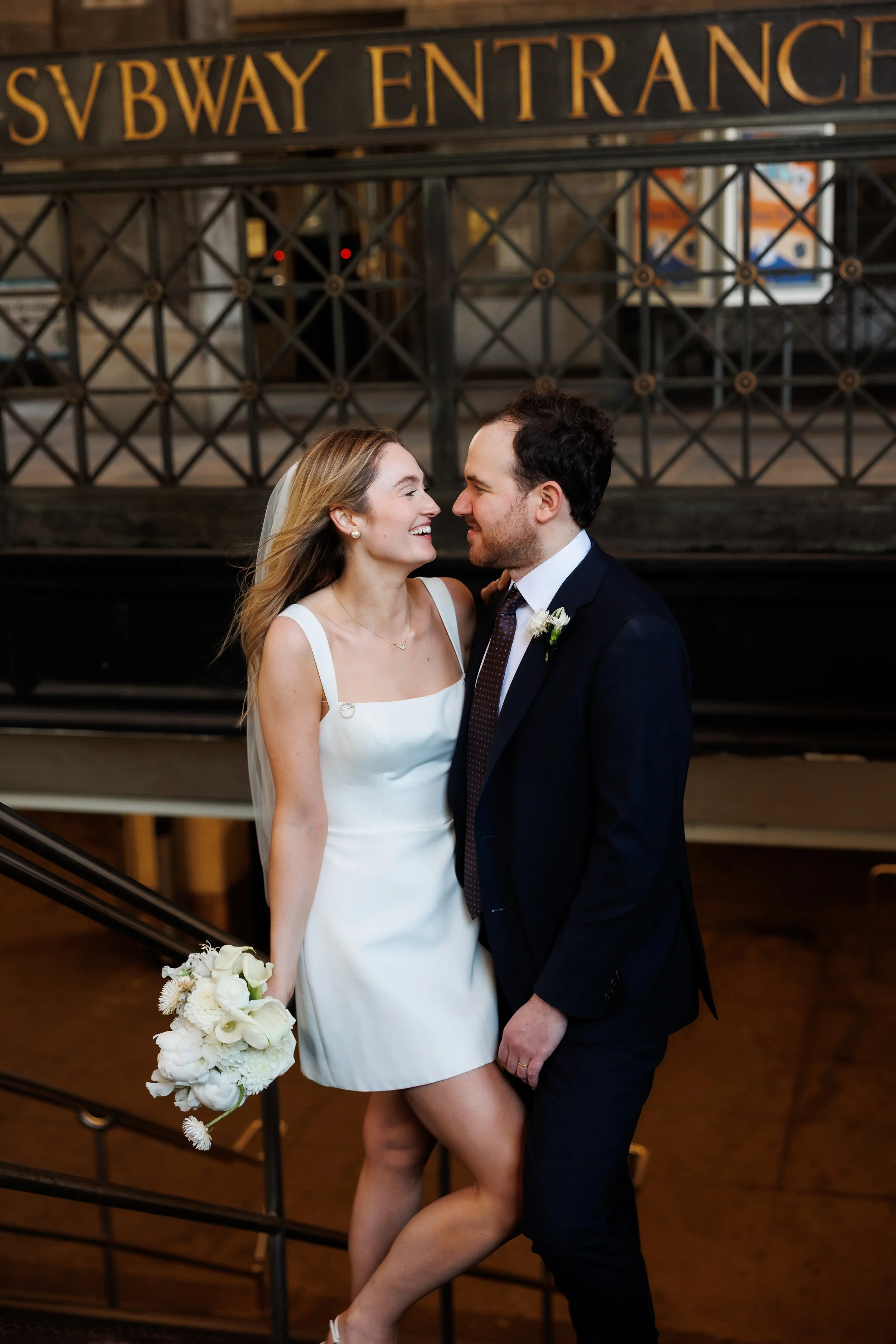 couple poses in front of subway entrance at the Brooklyn Bridge subway station after their NYC marriage bureau ceremony