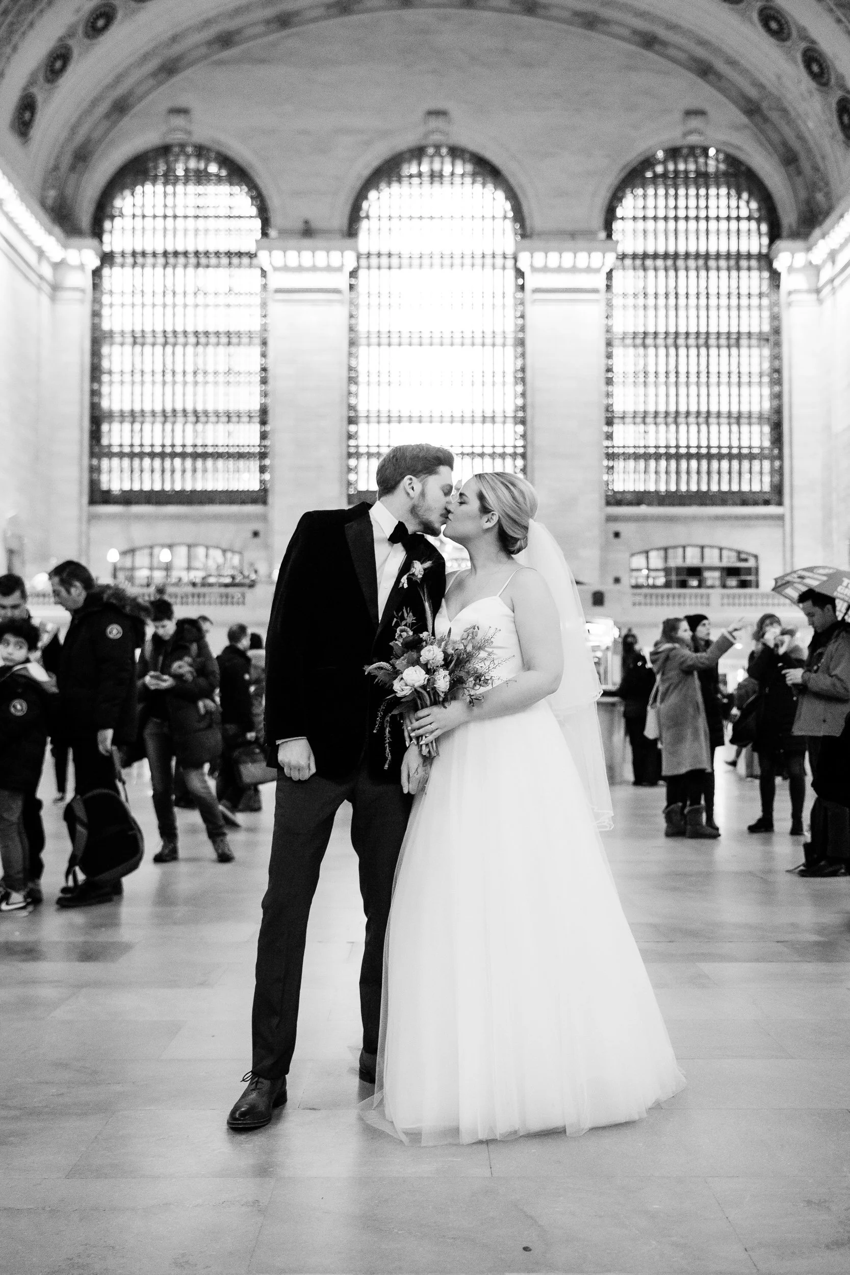 A newlywed couple kissing in the middle of a train station 