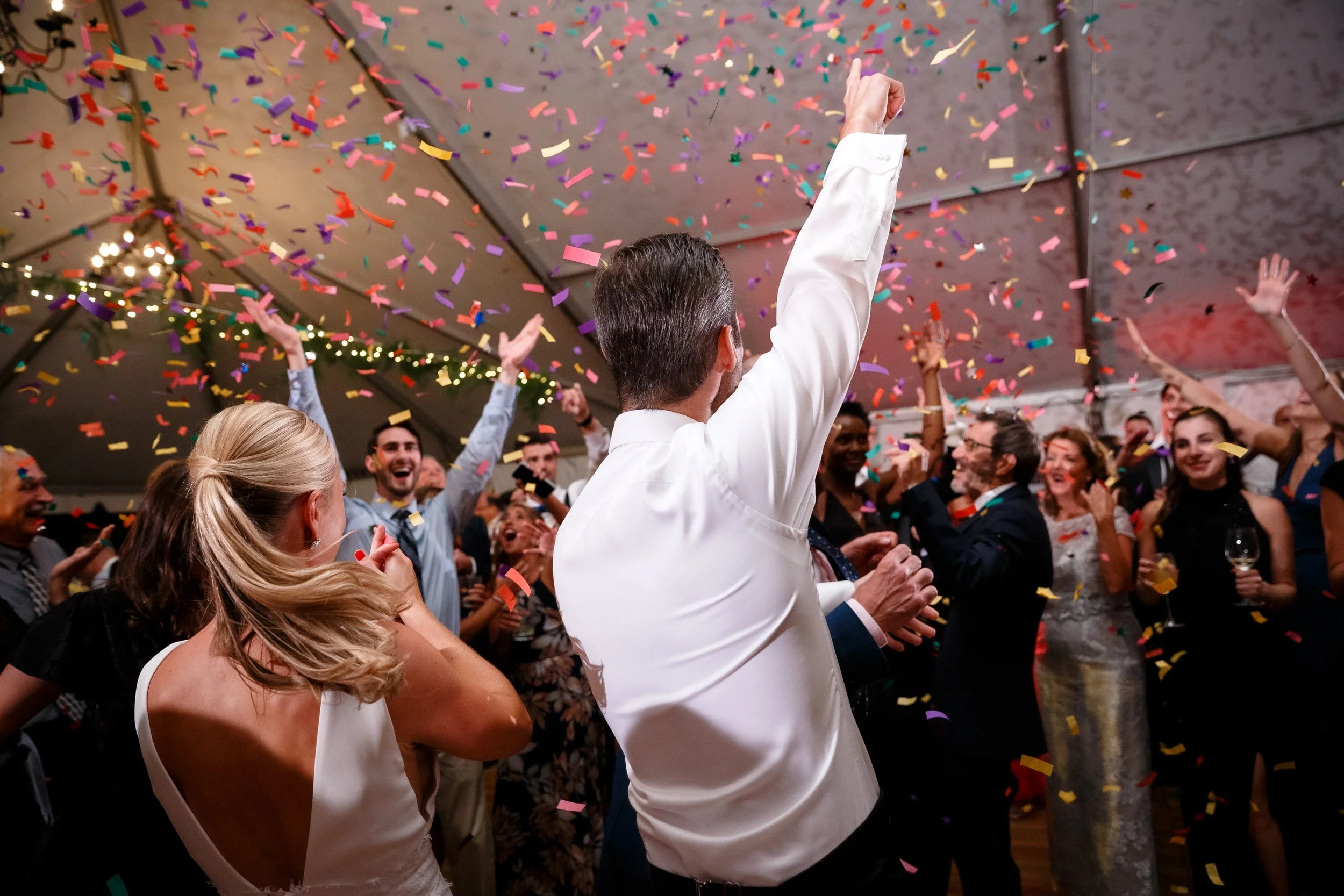 Newlyweds and wedding guests dancing under confetti at a wedding reception