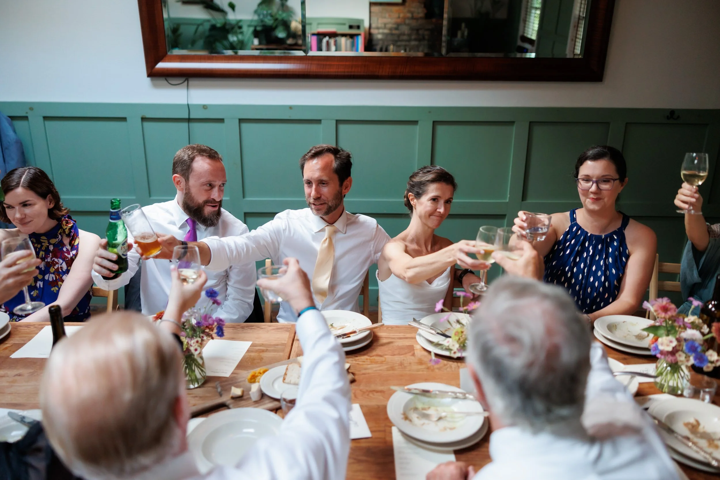 Newlyweds and wedding guests sitting around a table holding up their glasses in a toast 