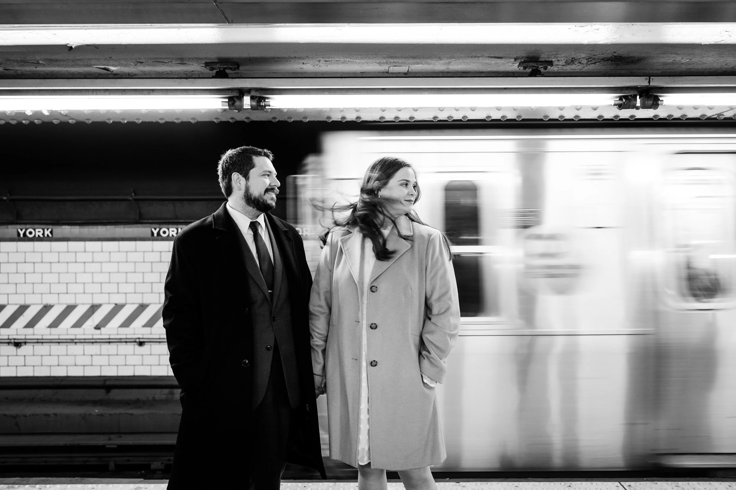 A wedding couple holding hands with a subway passing behind them 