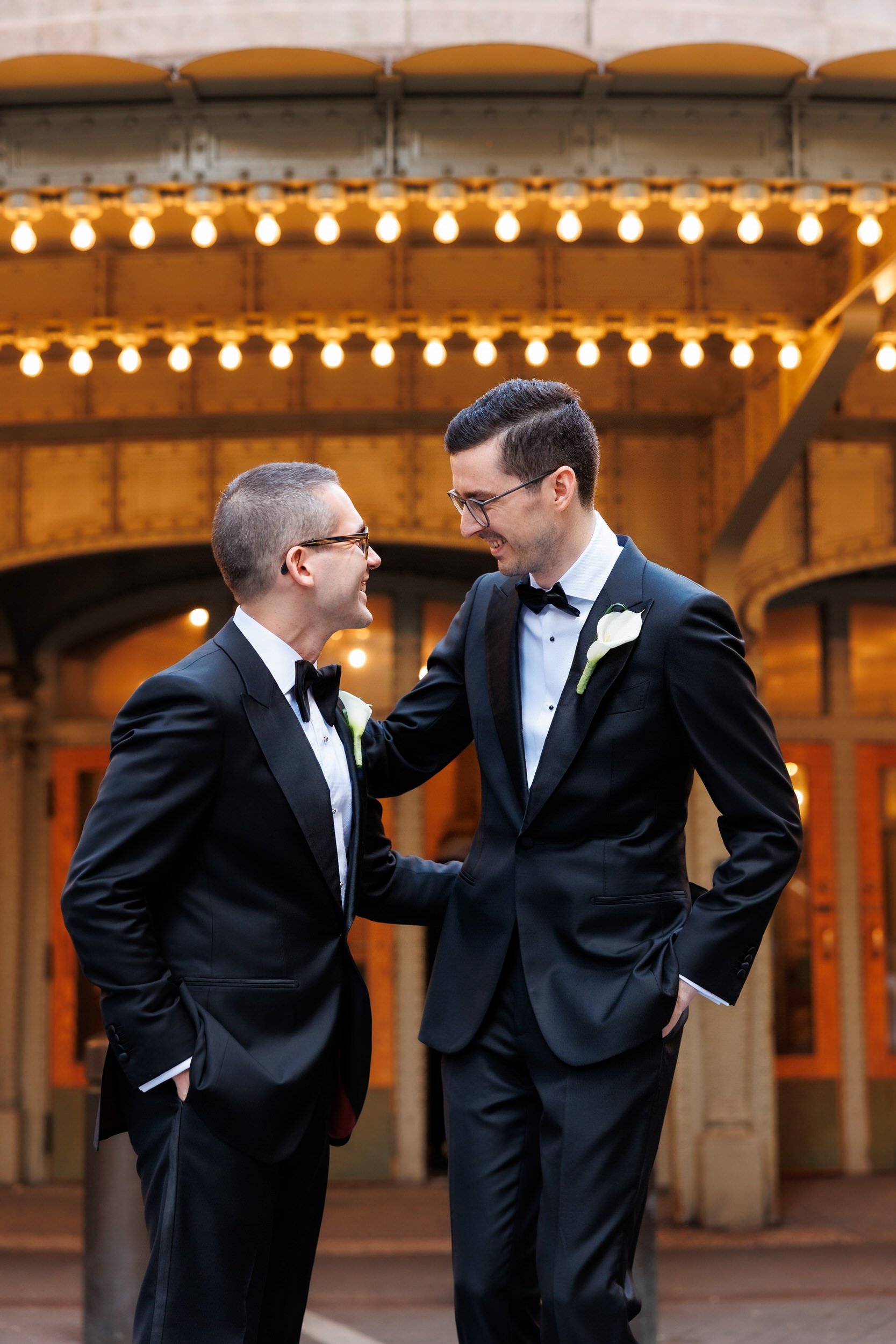 Two people in suits with their arms around each other laughing 